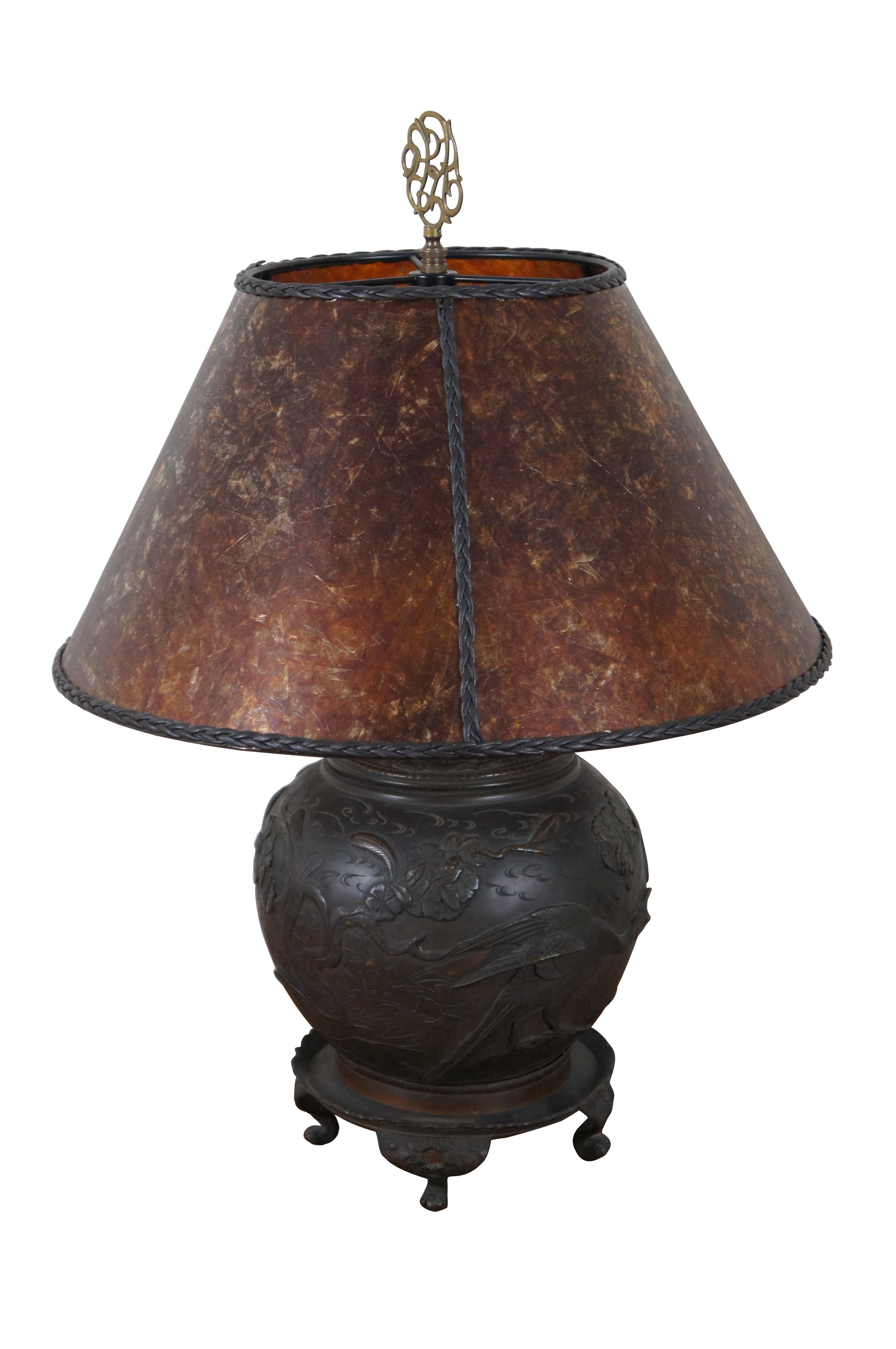 20th century Japanese cast bronze table lamp in the shape of a ginger jar / urn sitting on a footed pedestal, cast with a relief of blossoming cherry trees and cranes. Paired with a translucent multi-toned amber shade trimmed in black braid.