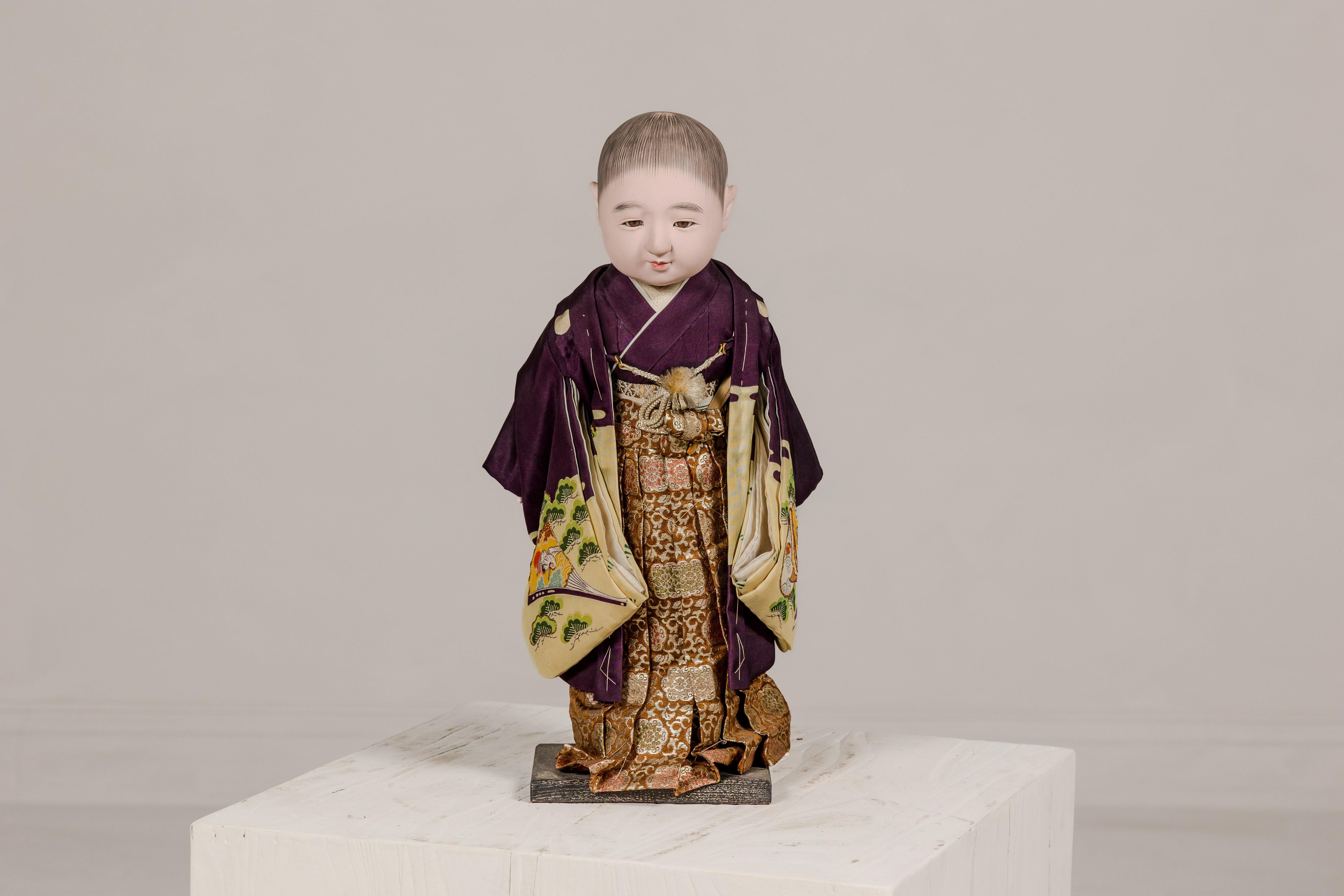 A Japanese Ichimatsu doll depicting a little boy wearing a city kimono. Step back in time and embrace the captivating charm of this vintage Ichimatsu doll, crafted circa 1950. Depicting a little boy adorned in a vibrant city kimono, this doll