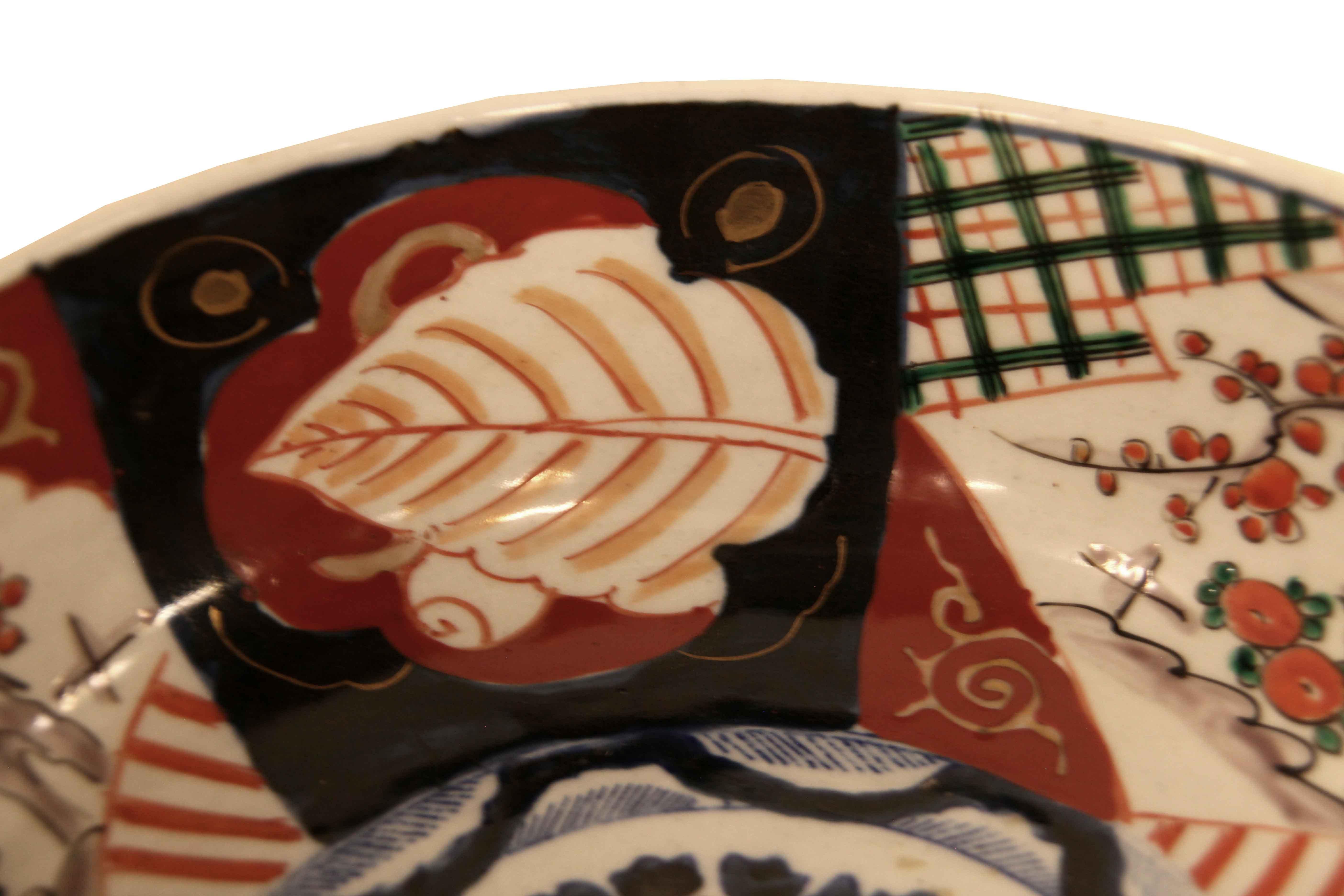 Japanische Imari-Schale, der innere Rand mit sich wiederholendem Muster aus stilisiertem Blattwerk, umgeben von einem marineblauen Grund in einer Kartusche, gefolgt von Bäumen und Blumen, die von einem Kreuzschraffur von grünen, schwarzen und