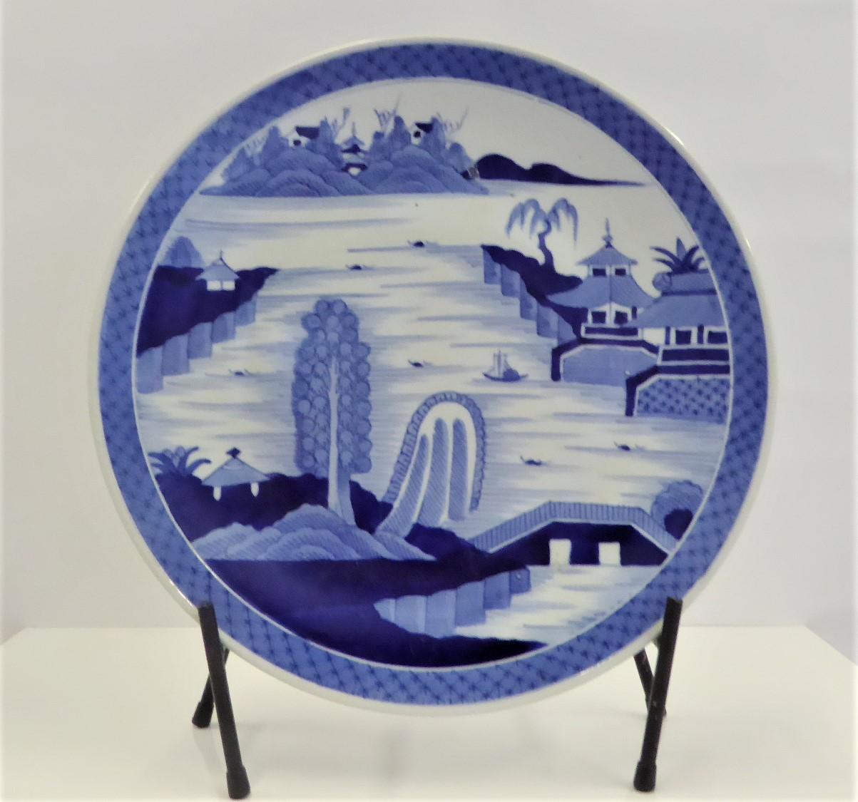 REDUCED FROM $650....Beautiful 1950s blue and white Japanese Imari charger depicting a serene hand painted scene of a village by river side with boats, a bridge and islands on the background. The rim in the back has stylized floral