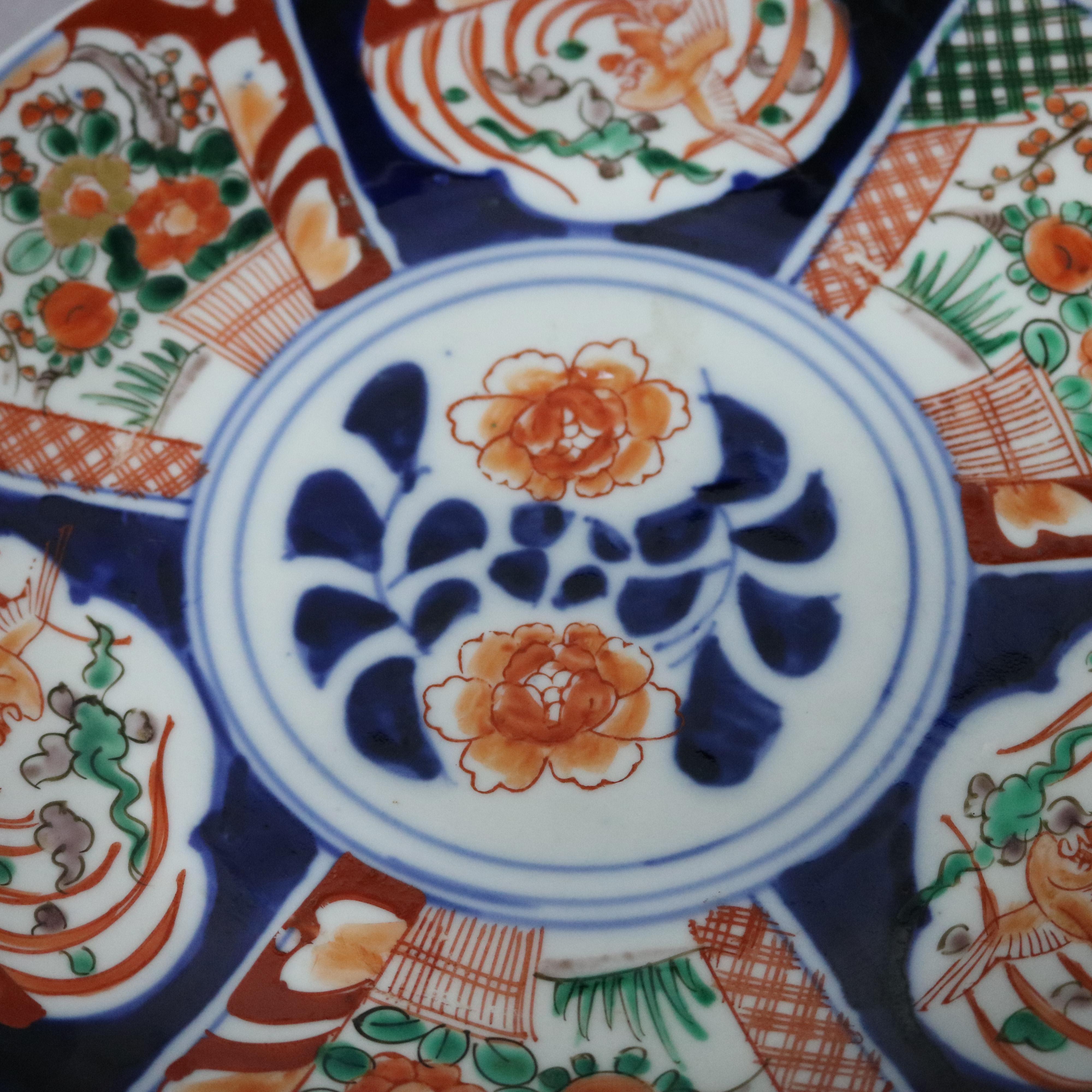 A Japanese porcelain charger offers hand enameled decoration including central floral spray and rim with alternating stereoptic panels of garden scenes and stylized phoenix, en verso blue decorated and incised maker stamp as photographed, 20th