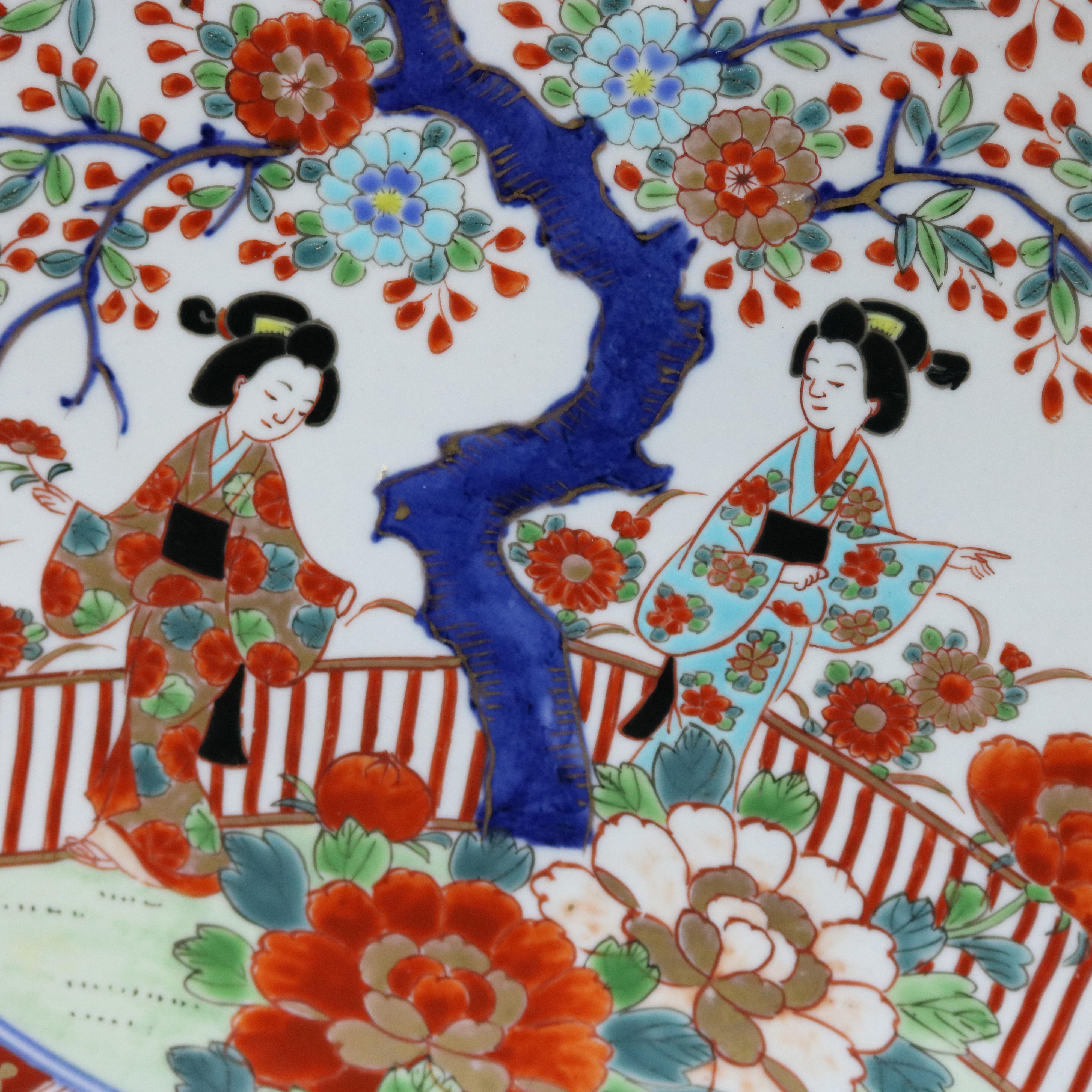 A Japanese Imari porcelain charger offers central garden scene with figures and tree with foliate decorated border, en verso chop marks and 