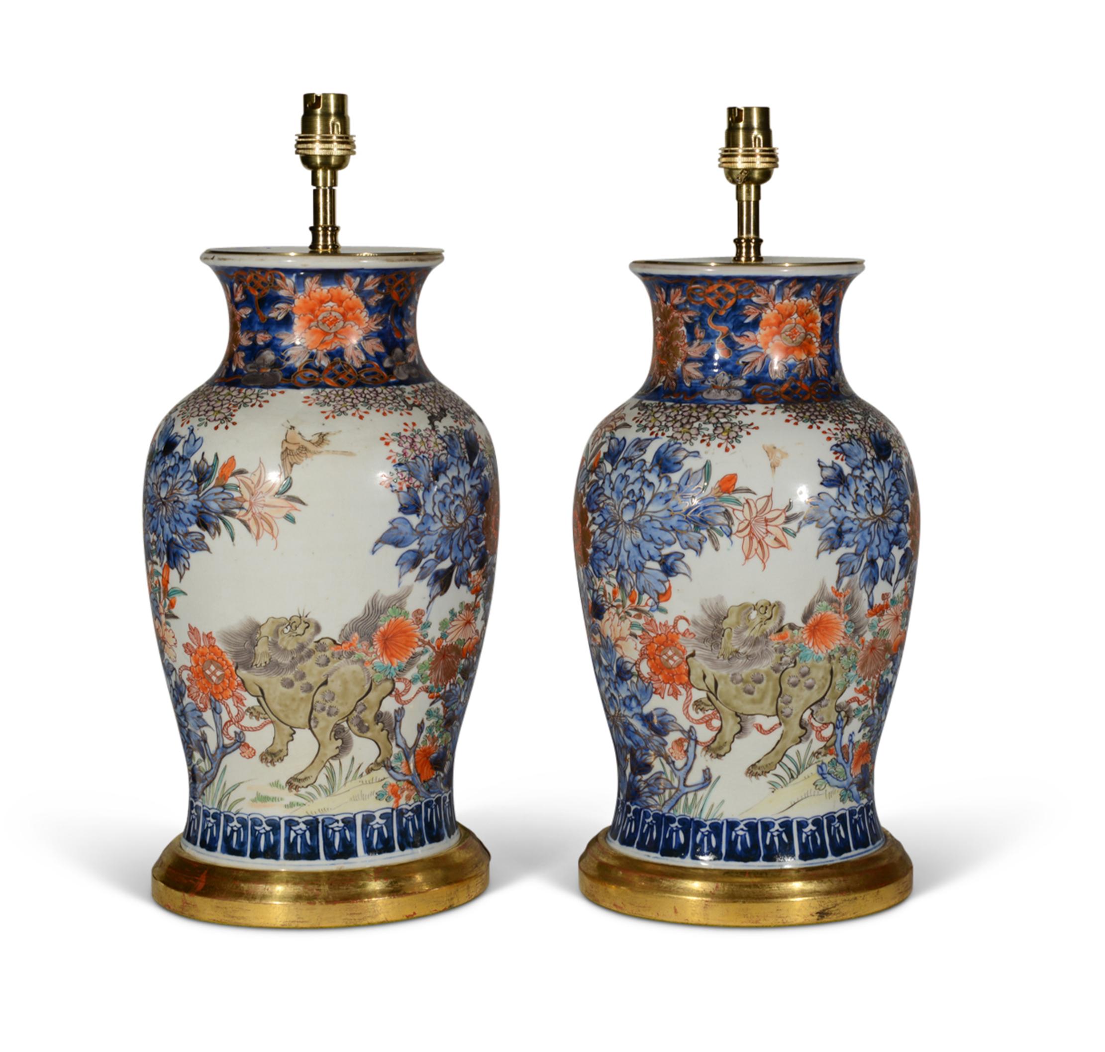 Fino par de jarrones Imari japoneses. Los cuerpos, en forma de balaustre, están decorados con paisajes continuos con Komainu flanqueado por densas flores de crisantemo y árboles en flor, en esmaltes azul bajo vidriado, rojo hierro y verde; los