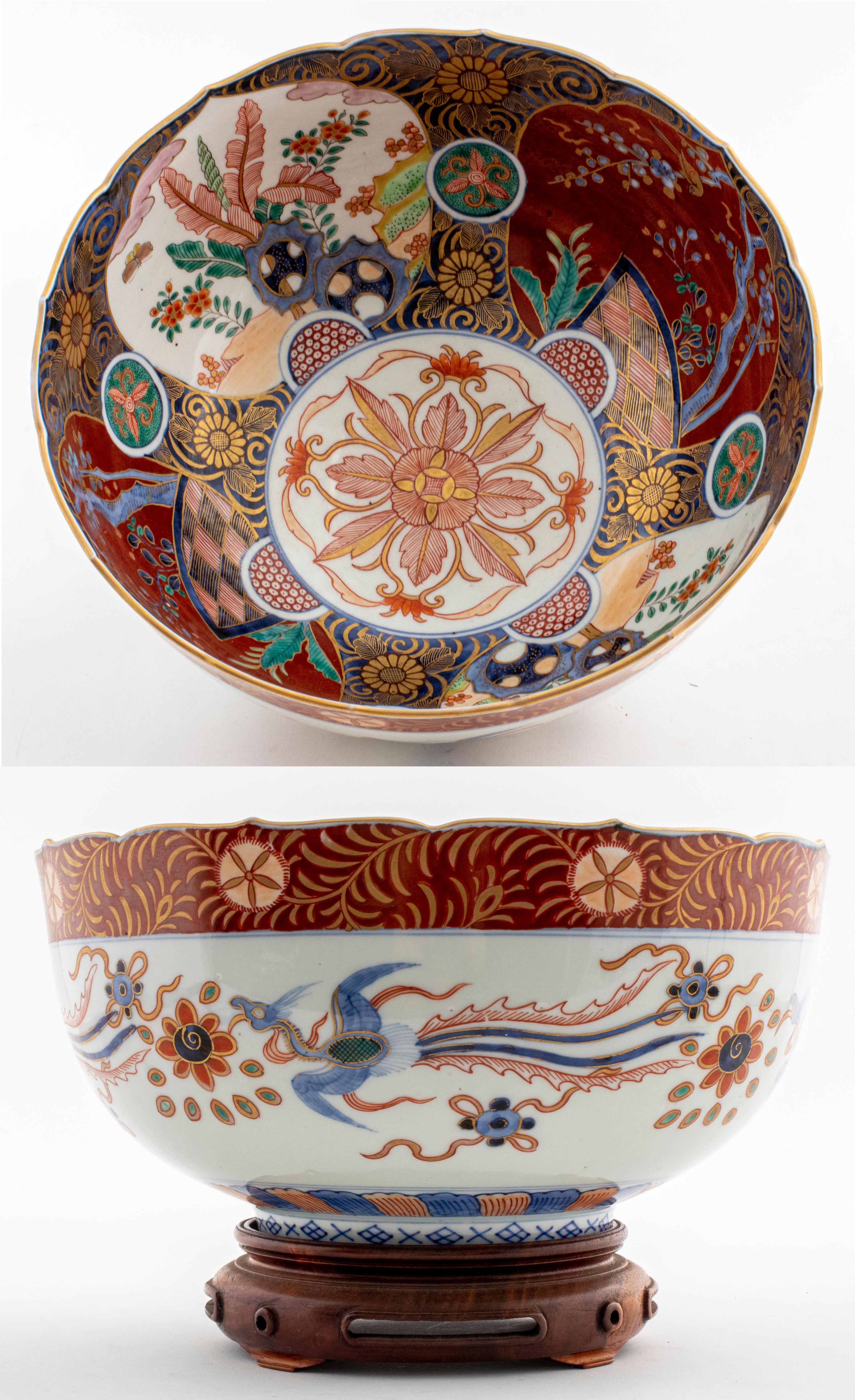 Japanese Imari porcelain bowl, painted and parcel gilt, with floral themed interior and flying phoenix birds on the exterior, on carved wood stand. Measures: 5.75