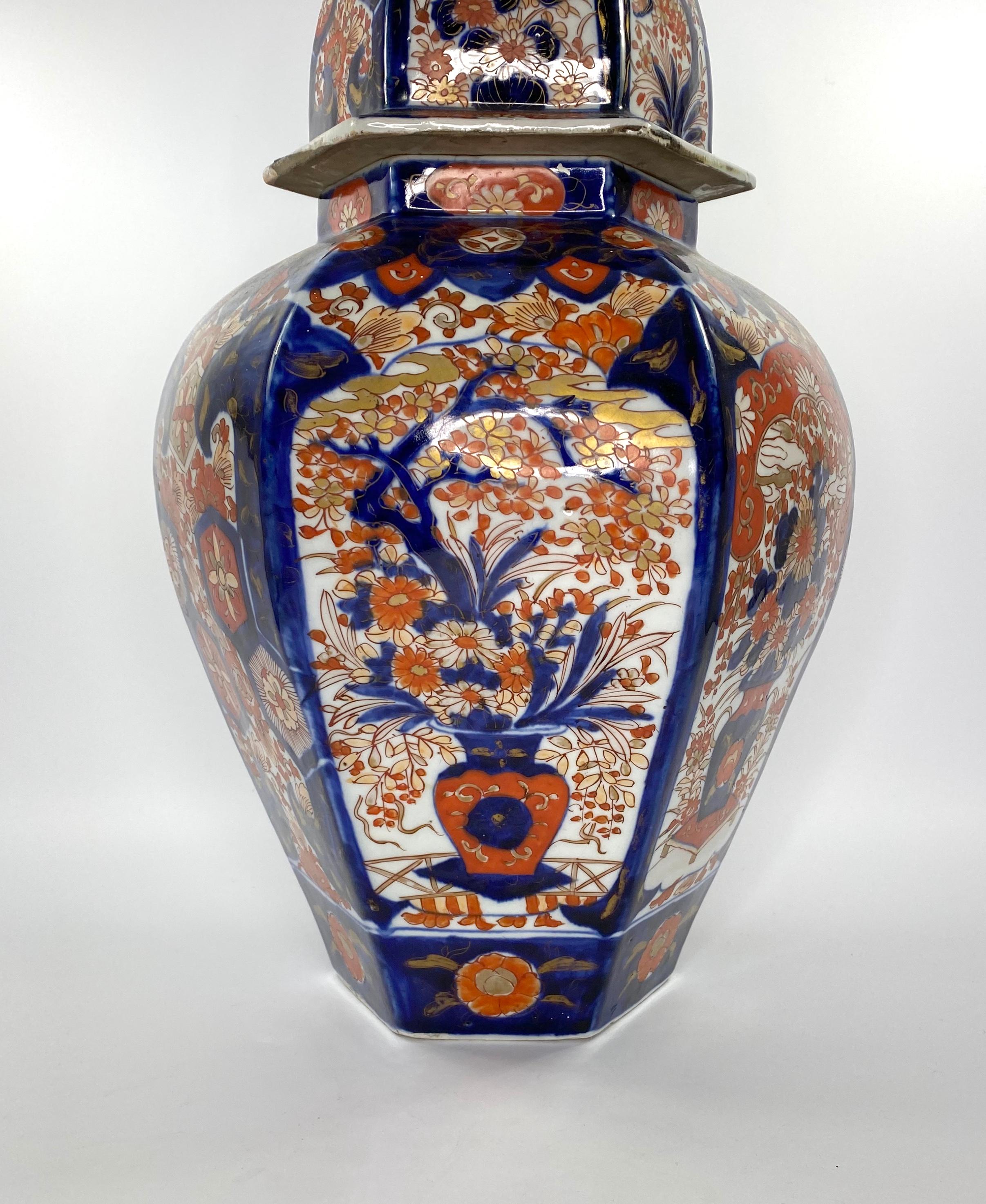 Japanese Imari porcelain vase and cover, circa 1890, Meiji Period. The hexagonal vase, painted with panels of flowering plants in vases, upon a low table.Two further panels of textile motif, upon a flowering ground. Lappet border to the shoulder of