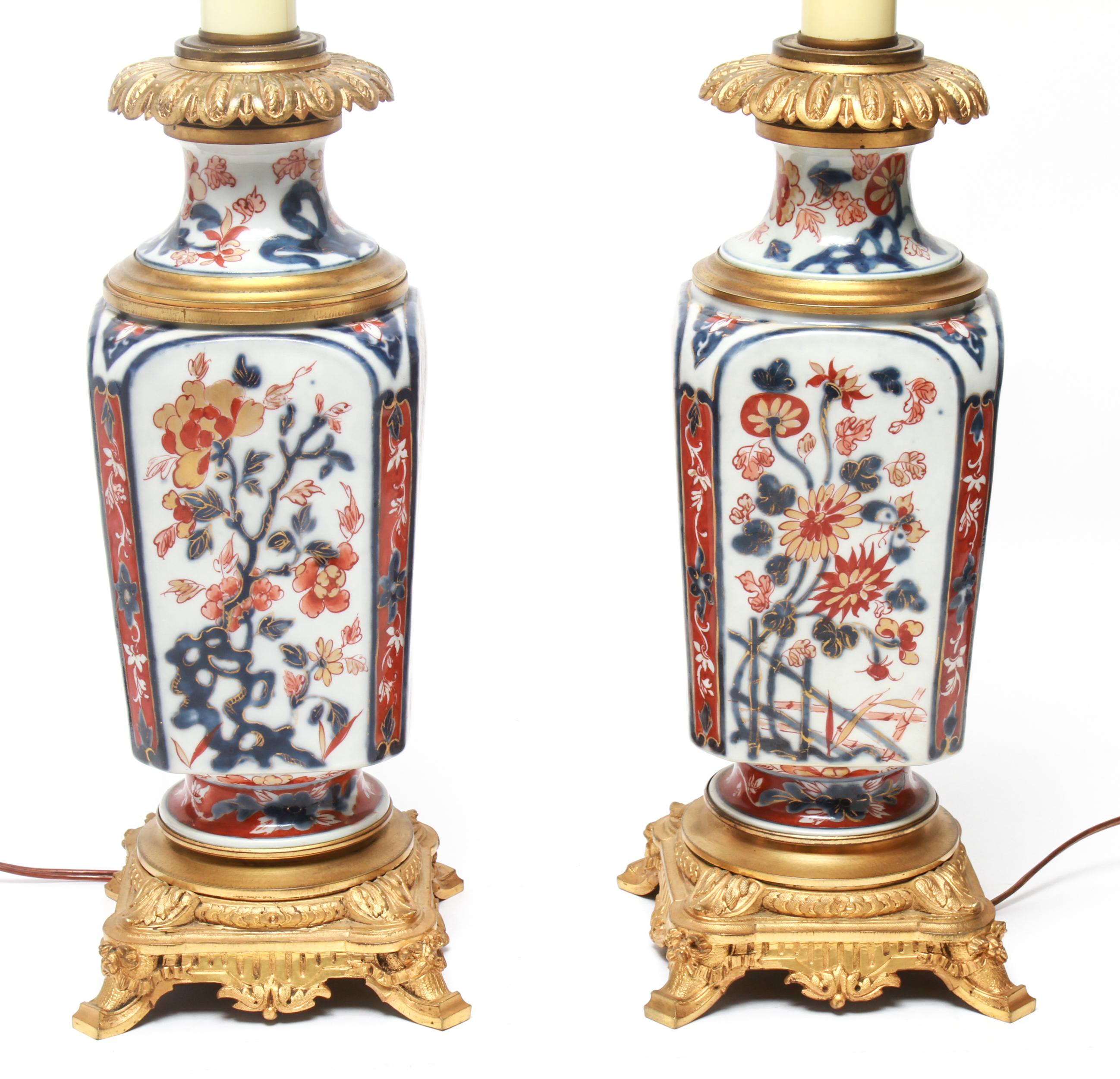 Japanese pair of Imari style porcelain table lamps, each featuring a scene with a phoenix above a vase of flowers and panels with floral designs. The pair sits on gilt brass mounts and has gilt brass collars. In great vintage condition with