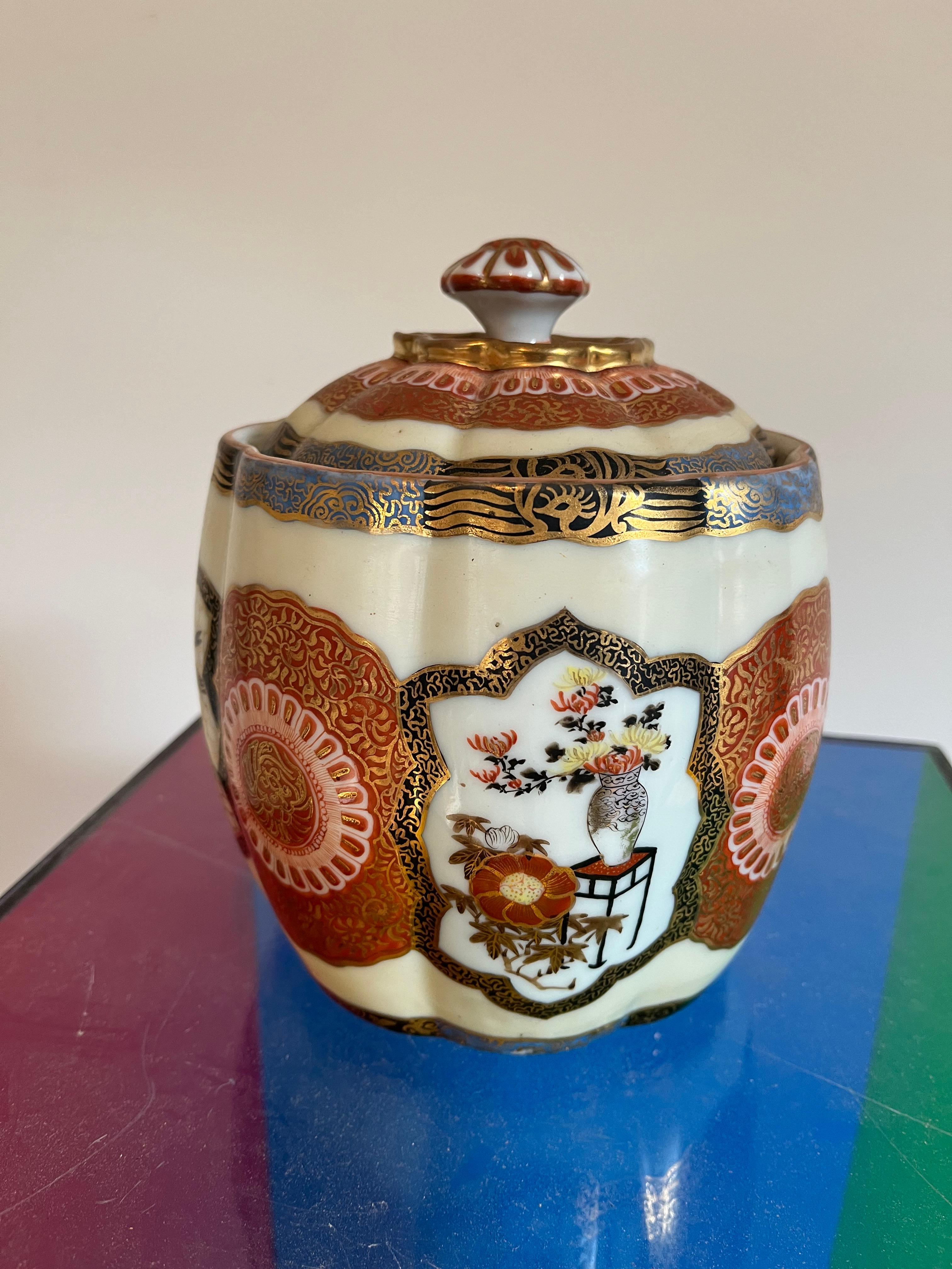A charming Japanese porcelain tobacco jar with lid in the Imari style, alternating panels showing still-life scenes and floral designs. Meiji period. The base shows the maker’s character marks in red. 
