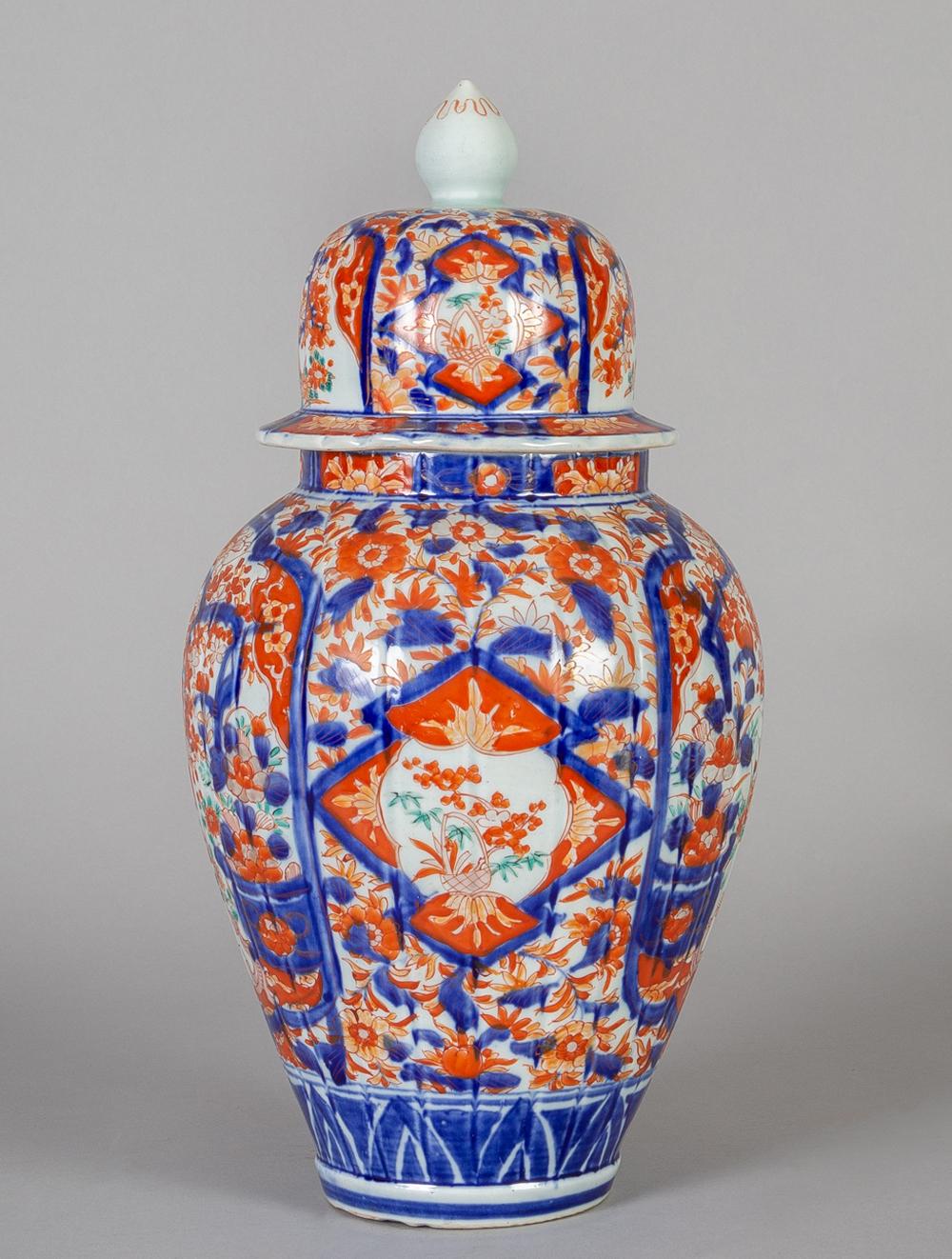 Large Japanese Imari lidded vase with ribbed body decorated with panels of flowering trees and a peacock-like bird perched on a branch, in polychrome colors of iron red and blue, the base decorated with a bold geometric pattern.