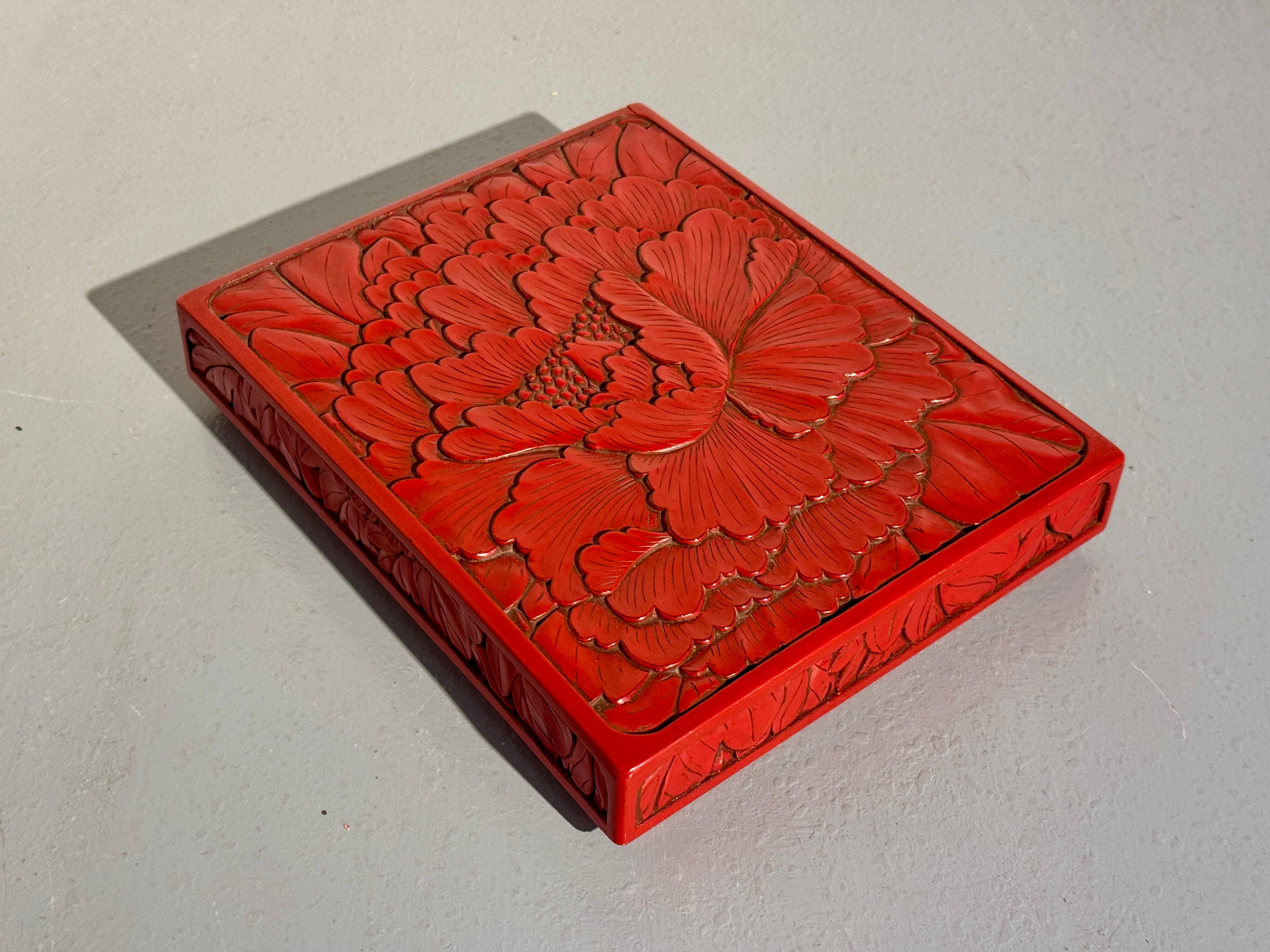 Un'attraente scatola di presentazione giapponese laccata di rosso Kamakura-bori con iscrizione, raffigurante una peonia, epoca Showa, metà del XX secolo, Giappone.

La scatola bassa e il coperchio sono intagliati con un disegno audace e sorprendente