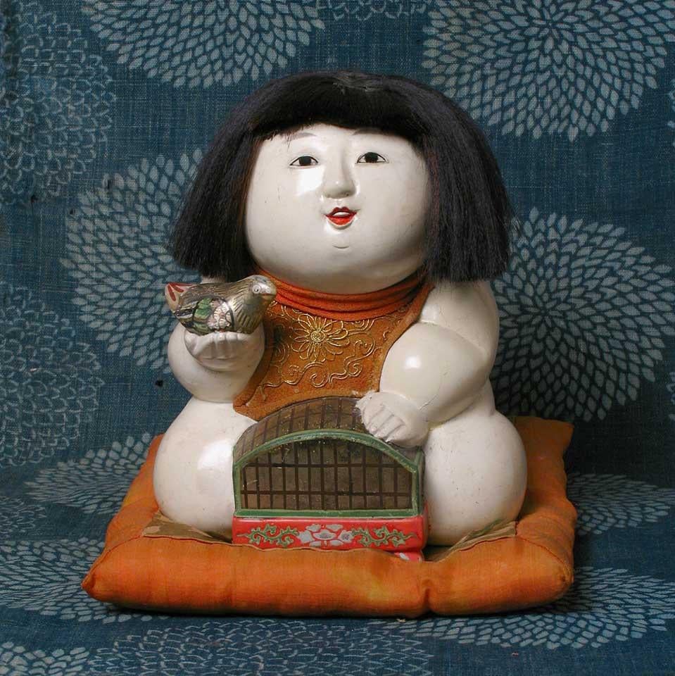 Japanese Kofuku-no-inori gosho ningyo (a good luck wish palace doll) of a plump kneeling male child holding a bird cage in front of him with a bird in the palm of his right hand, traditionally given amongst the nobility as a wish for freedom from