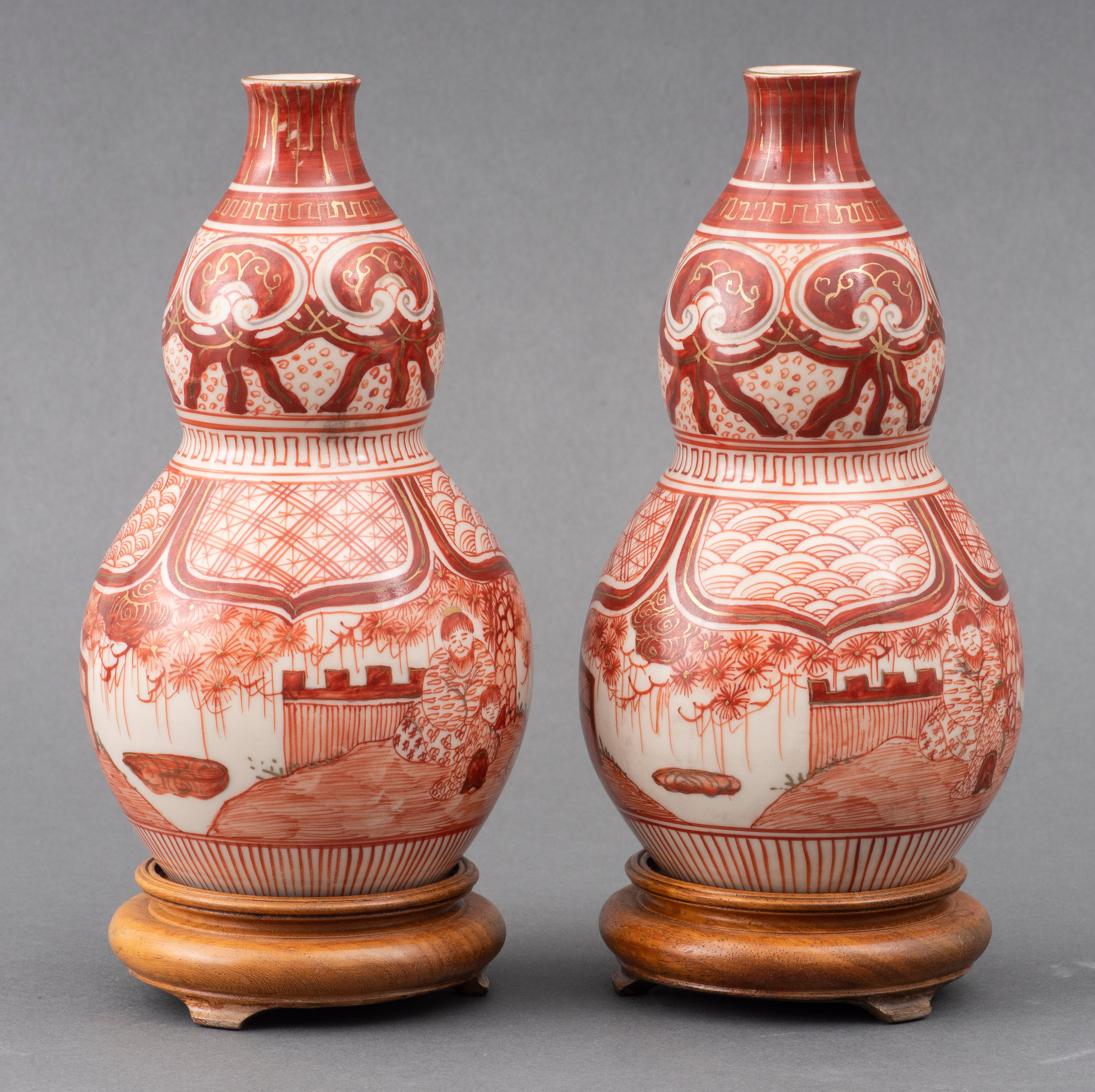 Paar eisenrot verzierte Doppelkürbiskrüge, japanische Kutani-Ware des späten 19. Jahrhunderts, fein verziert mit Figuren in einer Gartenlandschaft, vergoldeter Rand und gemalte Fuku-Marke auf dem Boden, jeweils mit Holzständer. 
Maße: 8