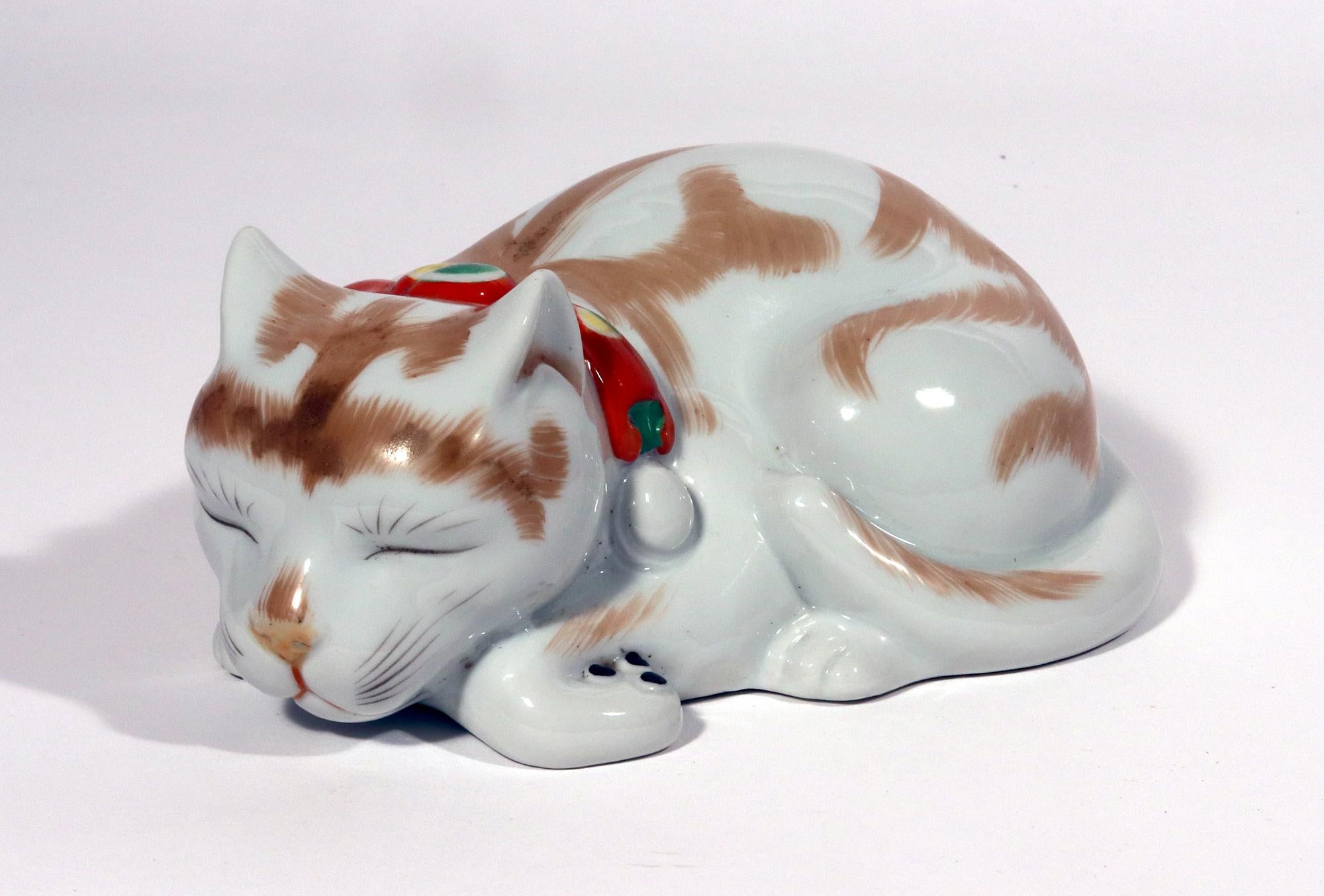 Japanese Kutani Porcelain Sleeping Cat Figure,
Meiji Period,
Circa 1910-20

The porcelain model of a cat depicts a cat naturalistically modeled with its paws beneath it and it tail folded over its hind quarters.  Around its neck is an orange collar