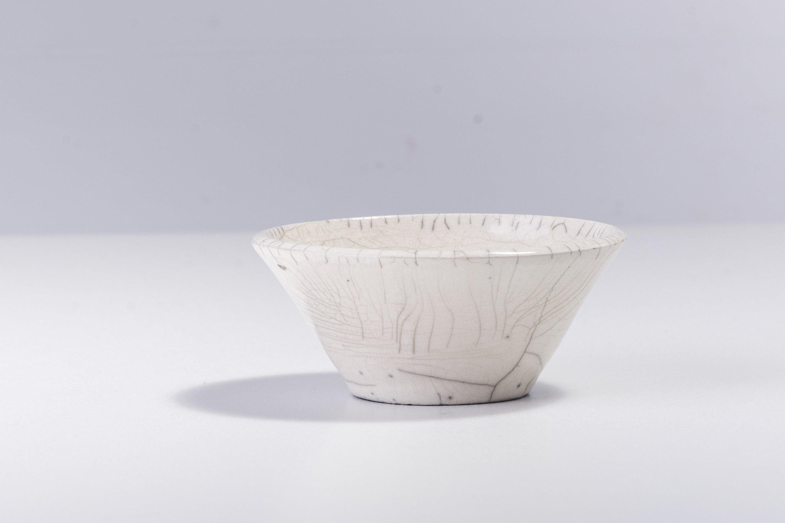 Design fonctionnel et technique sublime fusionnent dans ce bol spectaculaire, fabriqué à la main en céramique selon la technique japonaise de cuisson Raku nue. Cette pièce unique est ornée d'un patchwork sophistiqué de délicates fissures grises qui