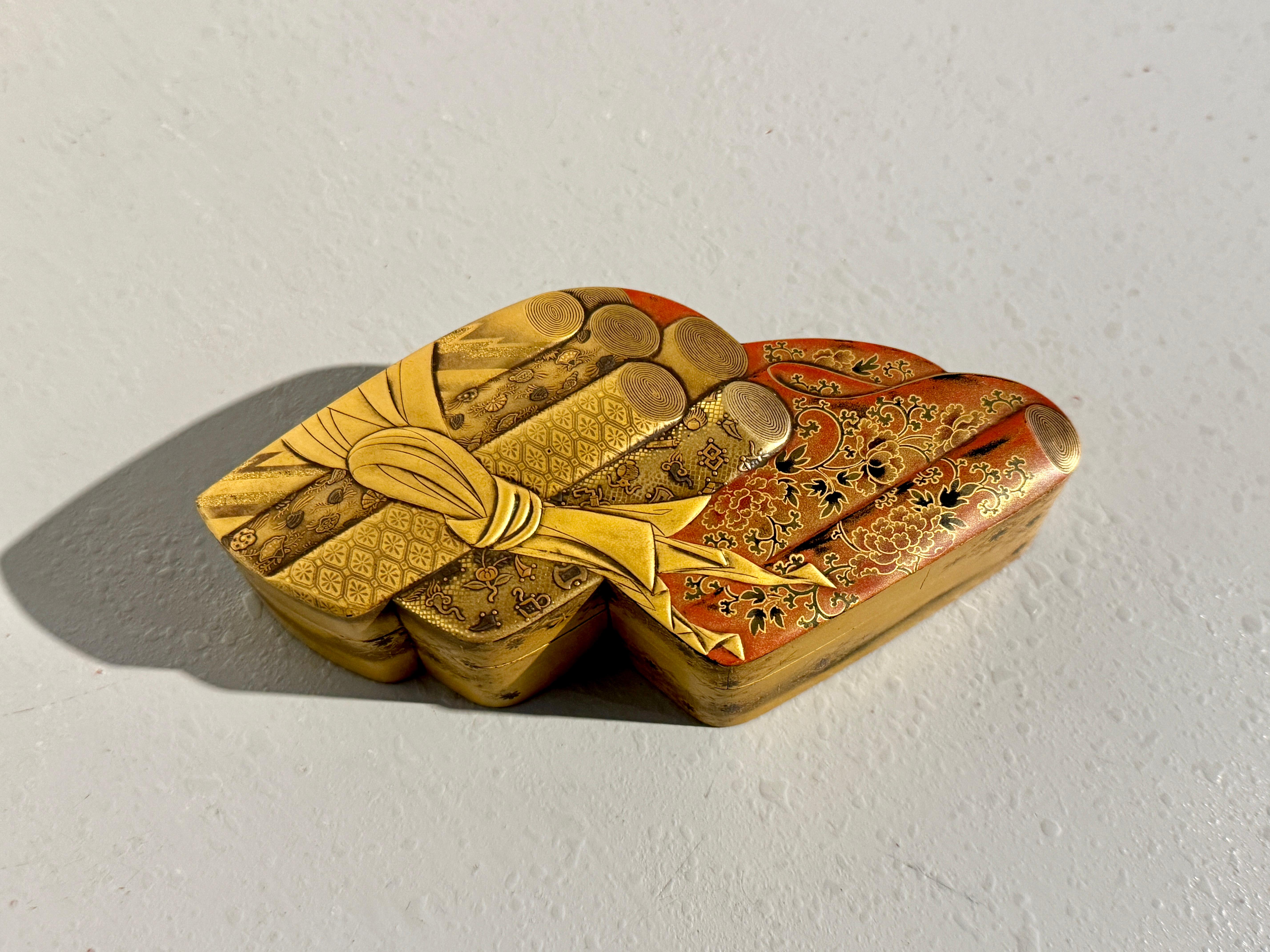 A very fine Japanese lacquer tebako, box for personal accessories, in the form of rolled bolts of brocade fabric, Meiji Period, late 19th century, Japan.

The box is whimsically shaped as bolts of sumptuous rich brocades tied together. The bolts