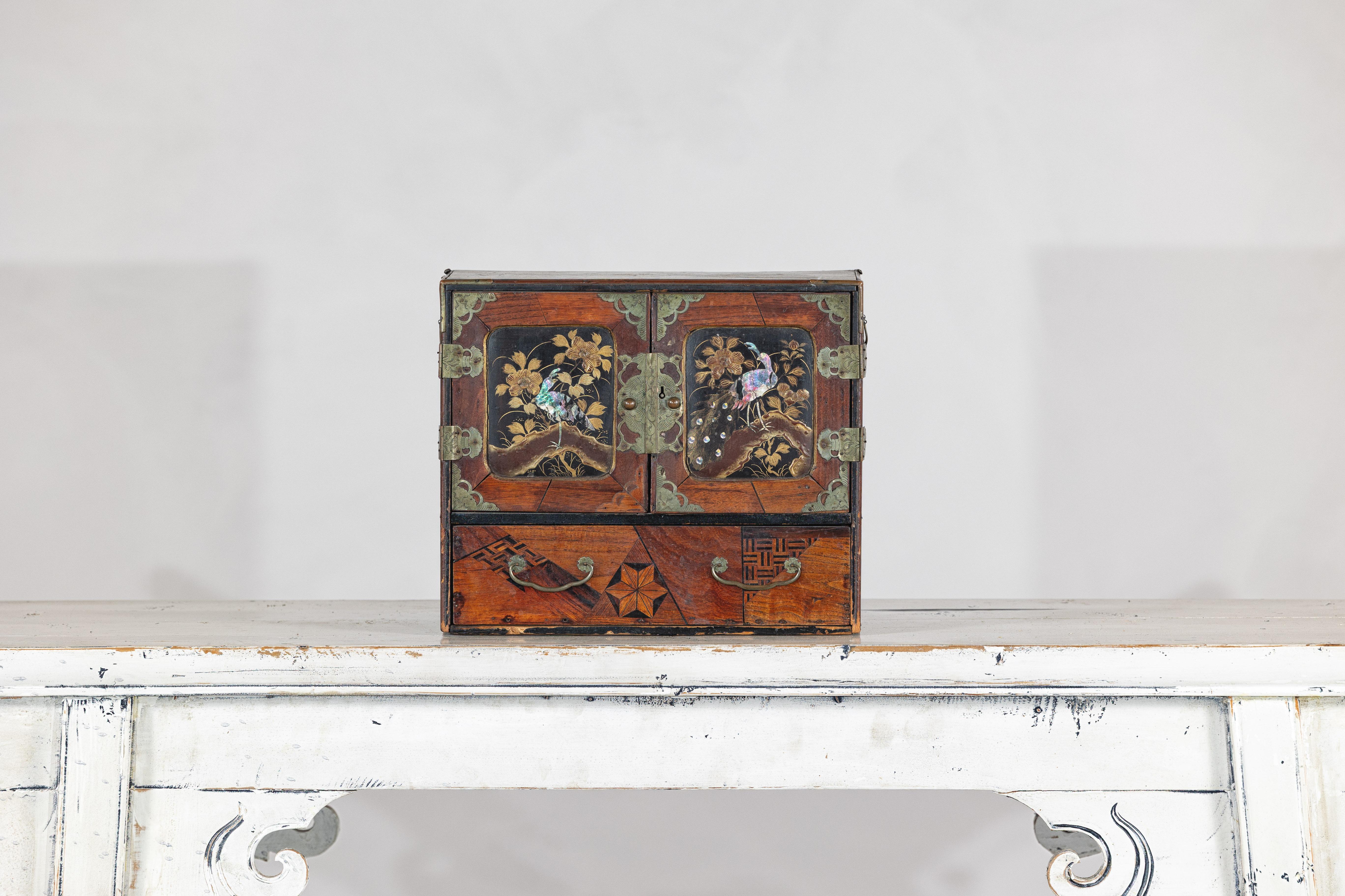 Este compacto mueble de sobremesa japonés de principios del siglo XX, finamente elaborado, está ricamente detallado con técnicas decorativas tradicionales y adornos de la época de la exportación. Las dos puertas superiores están adornadas con