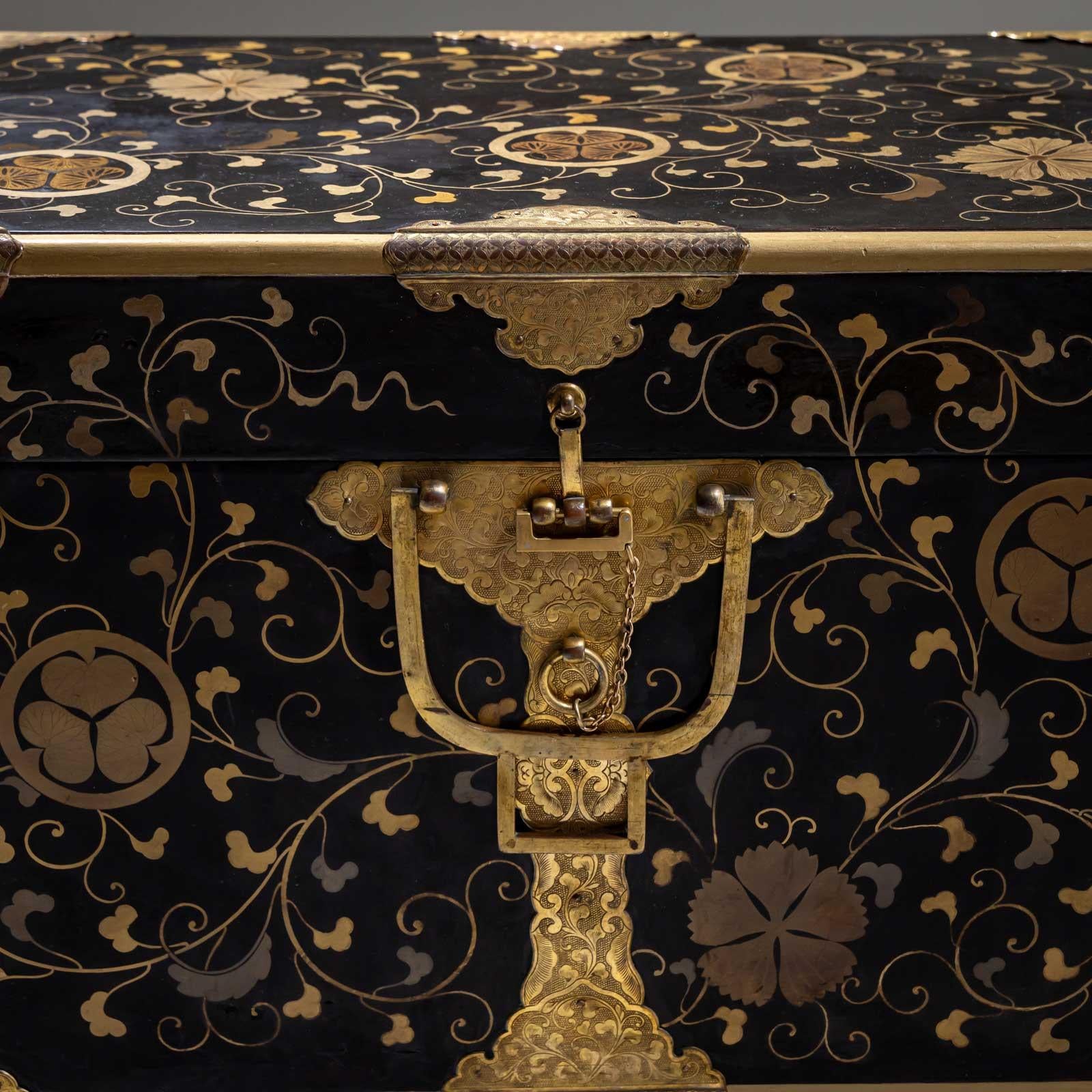 Pequeña arqueta rectangular japonesa con decoración lacada dorada en forma de zarcillos de hojas. El arcón está decorado con herrajes recortados y grabados ornamentalmente en las esquinas y alrededor de la cerradura de grillete. Estado restaurado. 