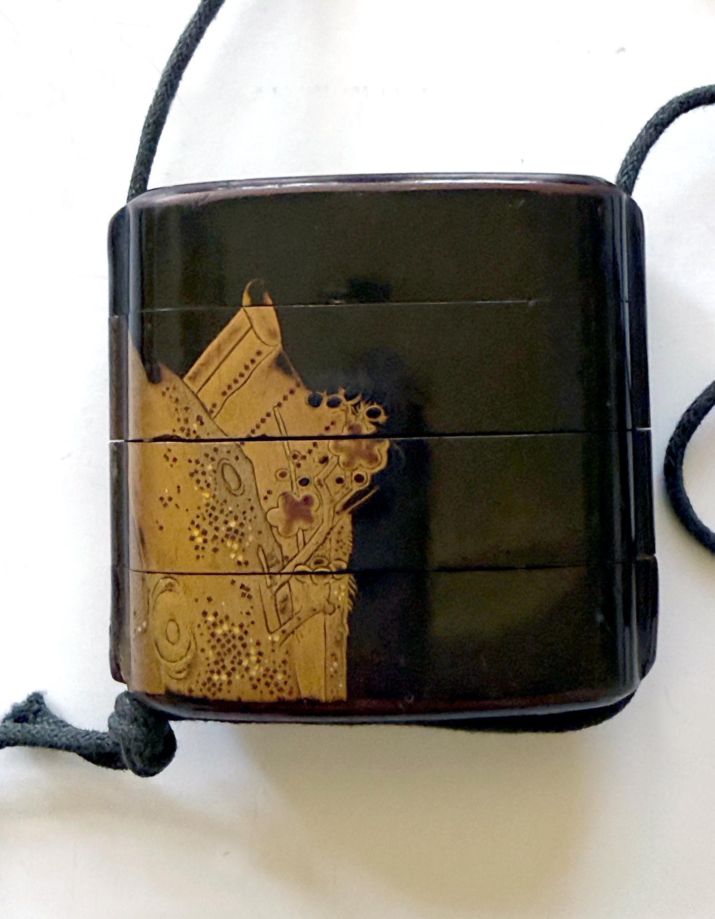 Un inro japonais à quatre boîtiers avec un netsuke en bois sculpté à cordes, vers le 19e siècle. L'inro a une forme presque carrée avec des coins arrondis. La surface est décorée de hiramaki-e et de kirigane dorés sur un fond laqué noir. D'un côté,