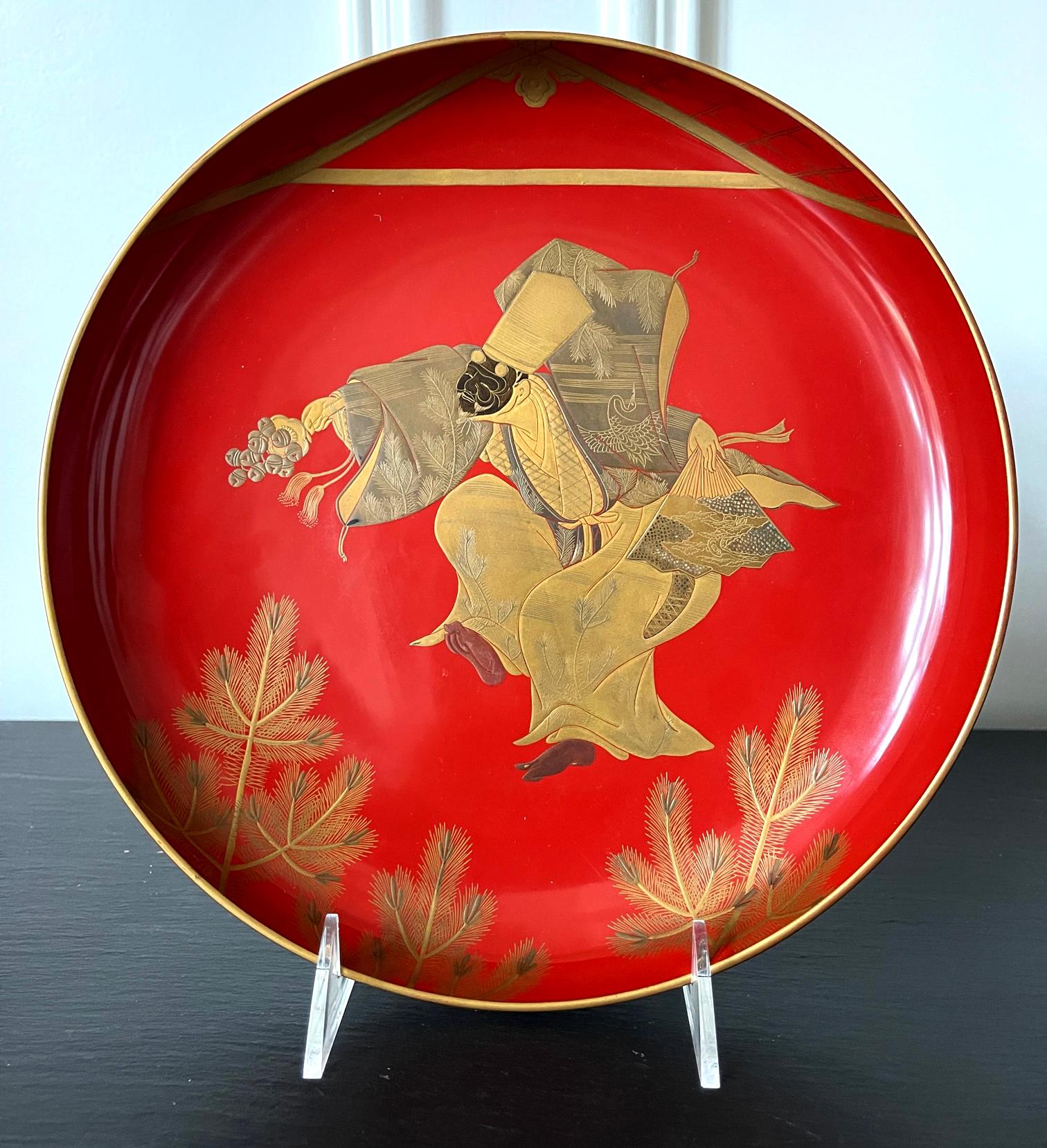 A large circular plate with a short stem base in Vermillion lacquer color from Late Meiji Period circa end of 19th century to early 20th century. The surface was decorated with a fine maki-e picture that depicts a masked dancer in motion. The figure