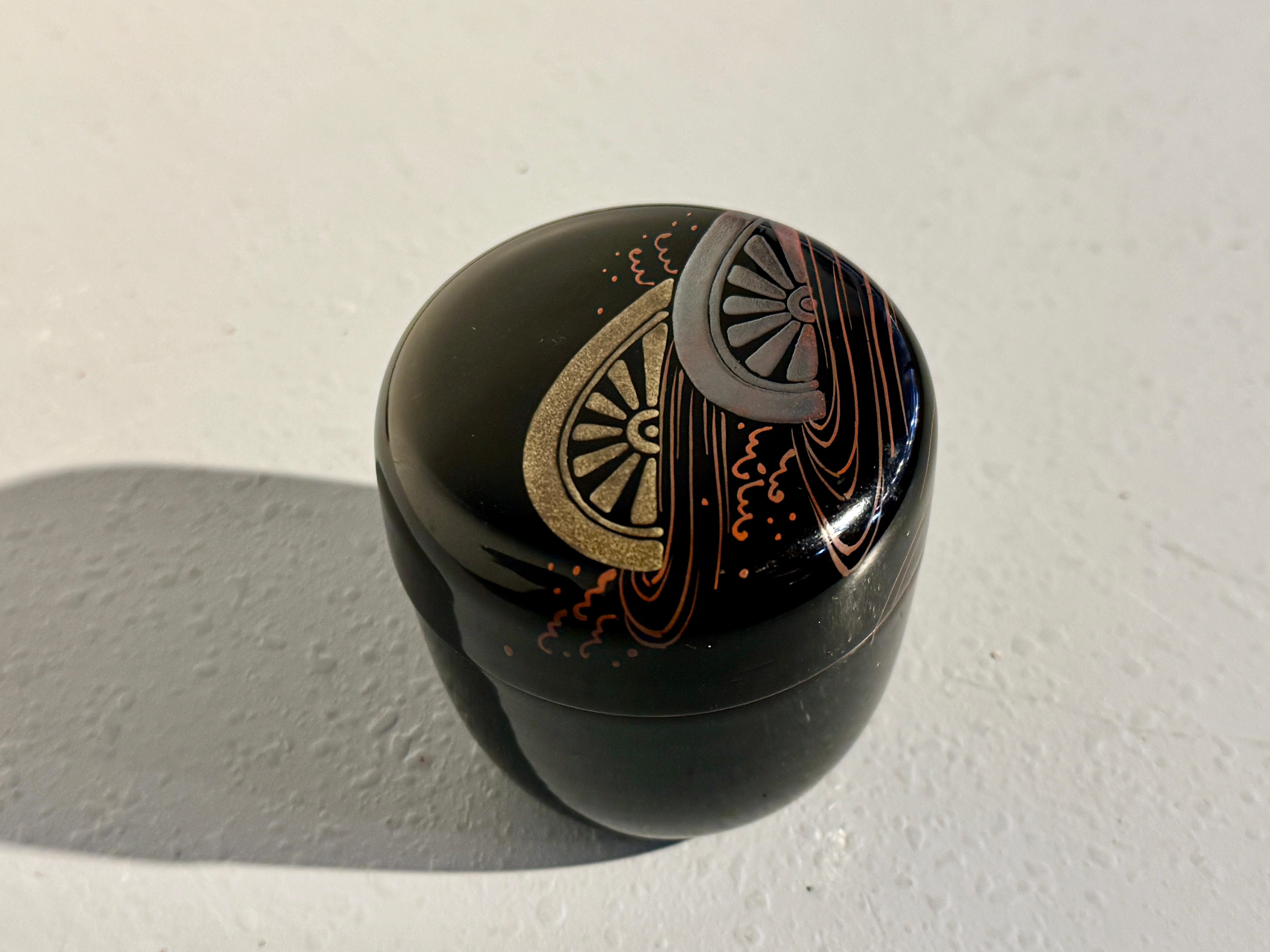 A refined Japanese lacquer tea caddy, natsume, with a maki-e design of soaking cart wheels, Showa Era, circa 1960's, Japan.

The elegant natsume of typical shape and covered in a black lacquer with taka maki-e . The cover with a striking raised