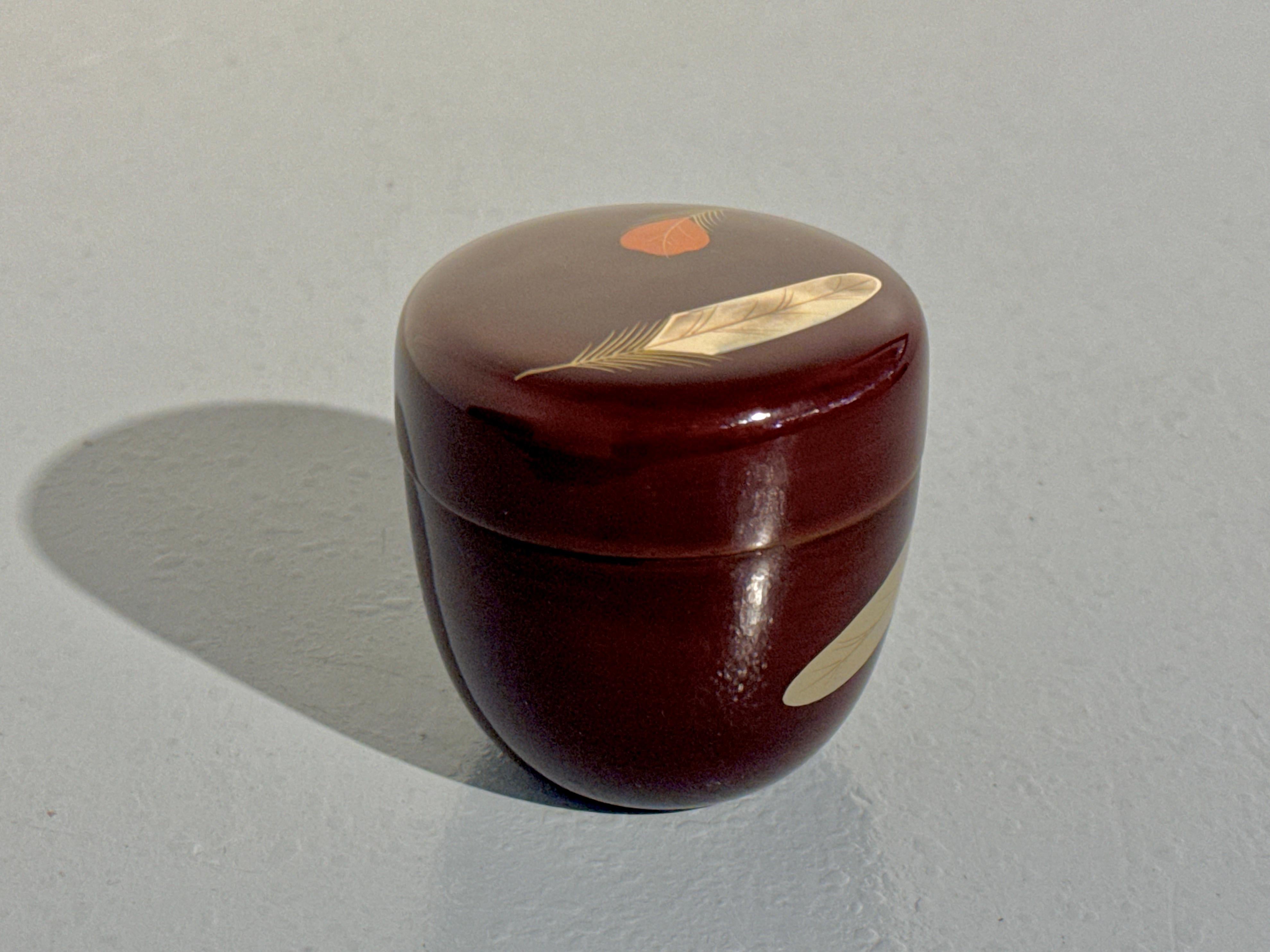 An elegant and refined Japanese lacquer tea caddy, natsume, with a design of feathers, Showa Period, mid 20th century, Japan.

The natsume is of typical form, covered with a semitransparent reddish brown lacquer. A design of three scattered feathers