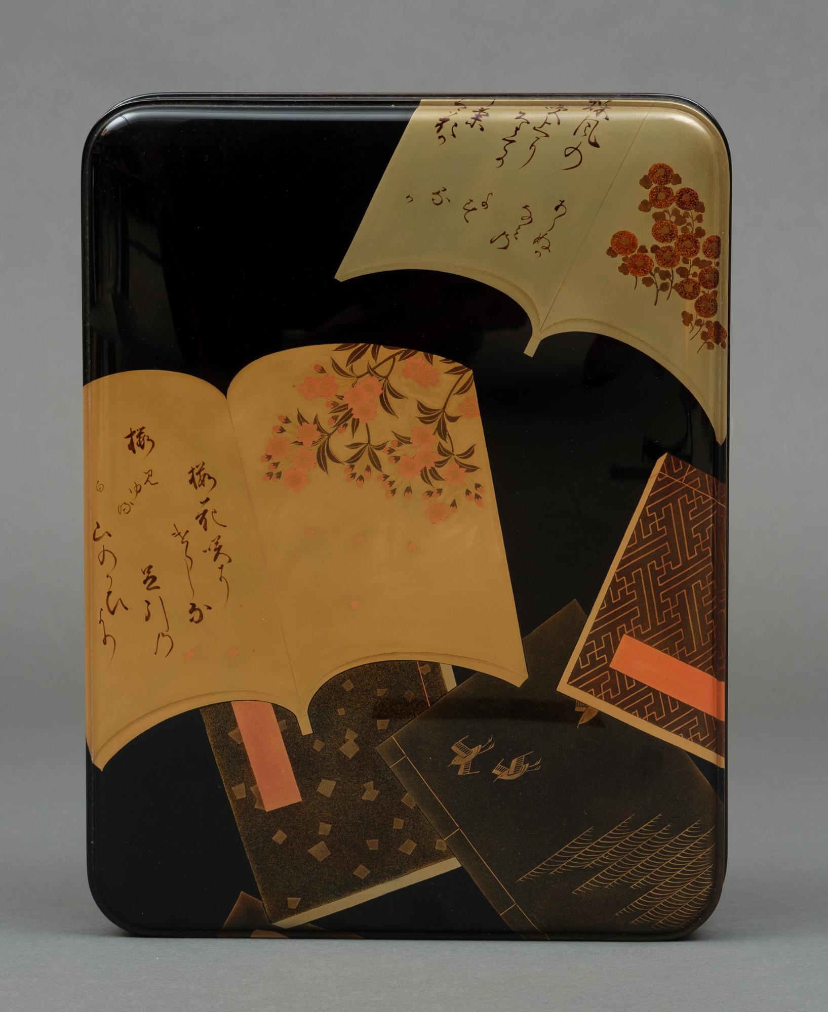 Superb rectangular black lacquer tebako (box for personal accessories) with a slightly domed well-fitted lid.

The lid has a continuous soft-tone multicoloured hiramaki-e (low-relief lacquer design) depicting several picture books (e-hon), of which