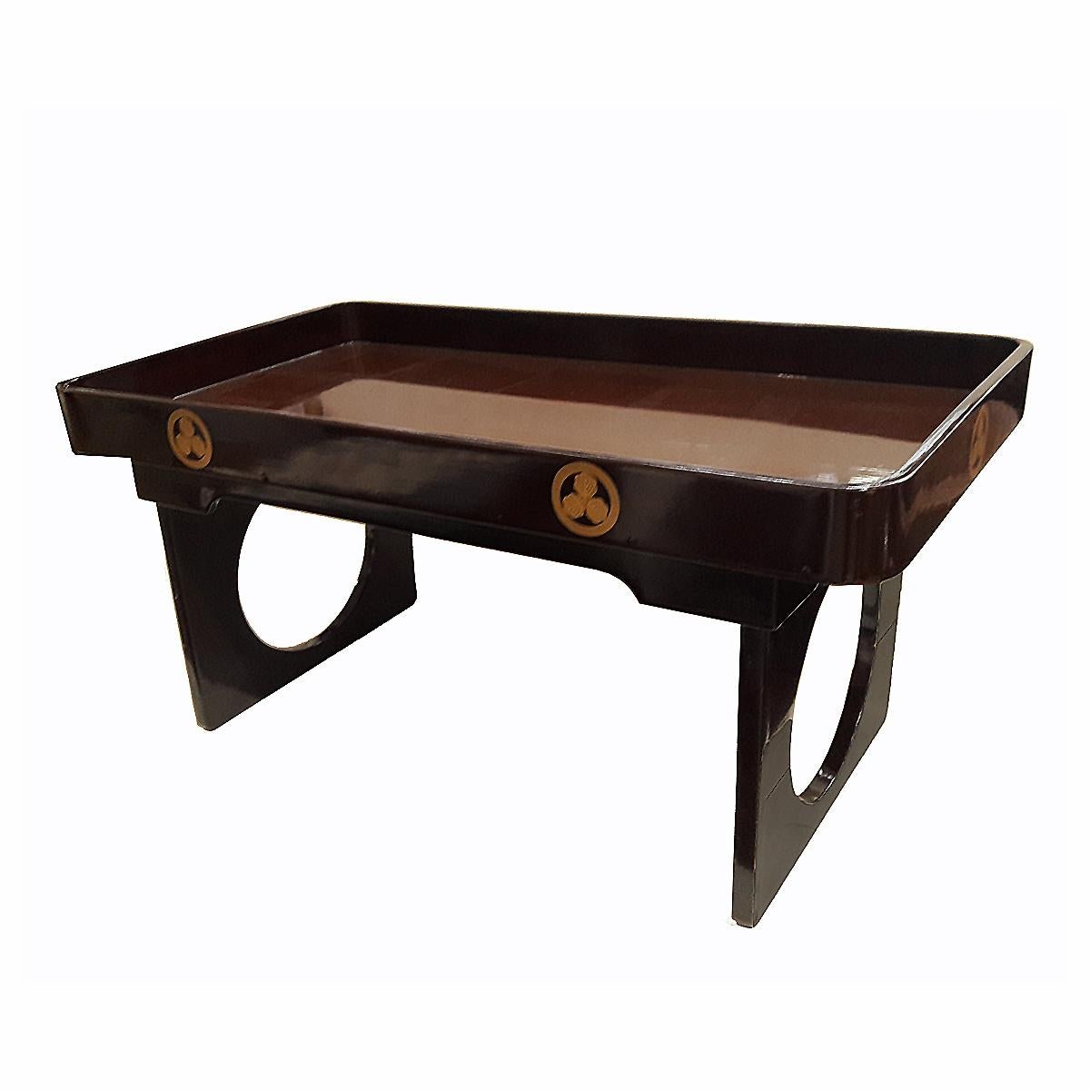 A charming and elegant folding tray table. Japan, early Showa period, circa 1940. 
Made out of wood, smoothly lacquered in brown color with golden accents, and a crafty folding mechanism that reflects the exquisite art of Asian wood joinery.