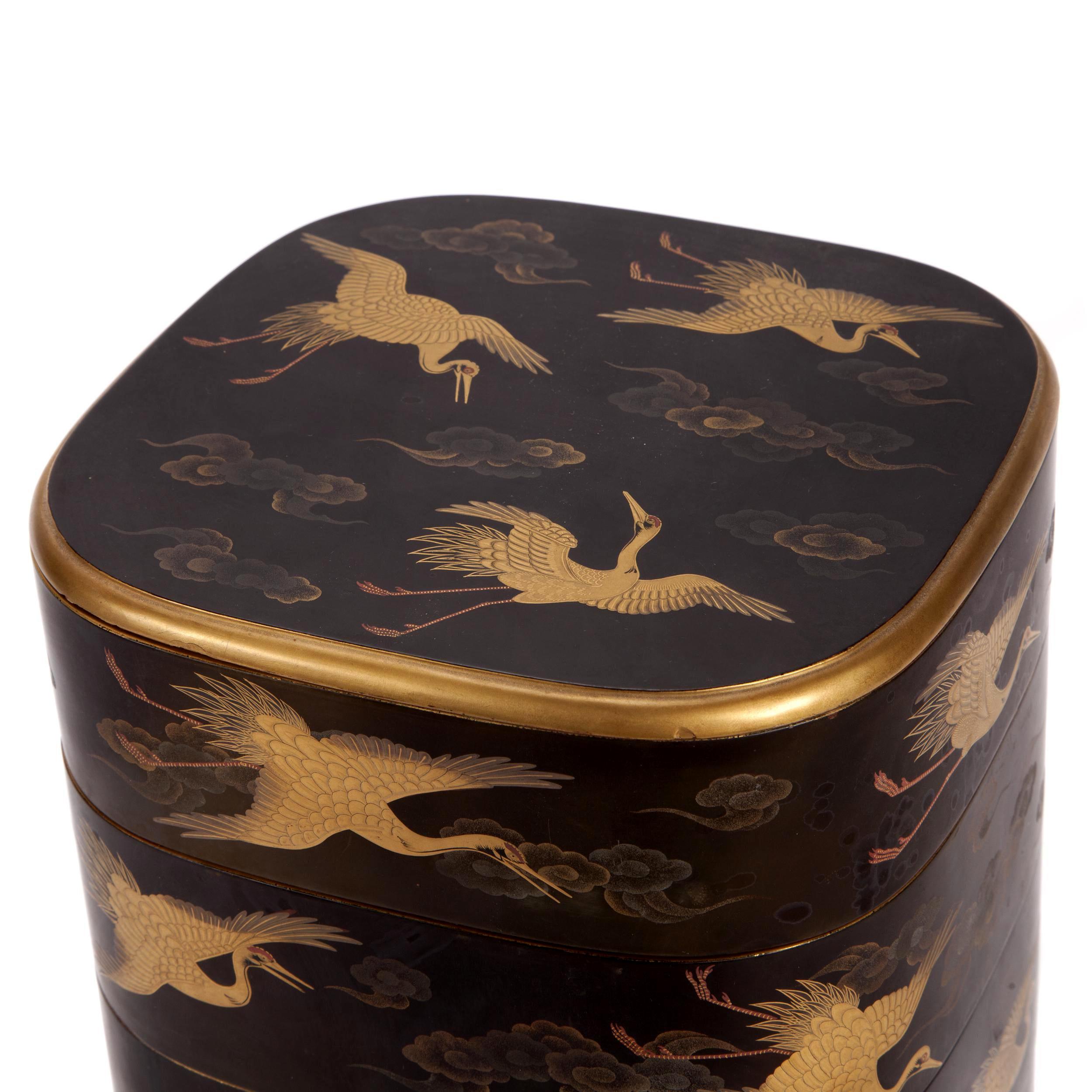 Japanese tier jubako box with four tiers circa early 20th century Meiji to Taisho period. The square boxes with rounded corner is finished in black urushi lacquer background. The surface was decorated with flying cranes among the scrolling clouds.