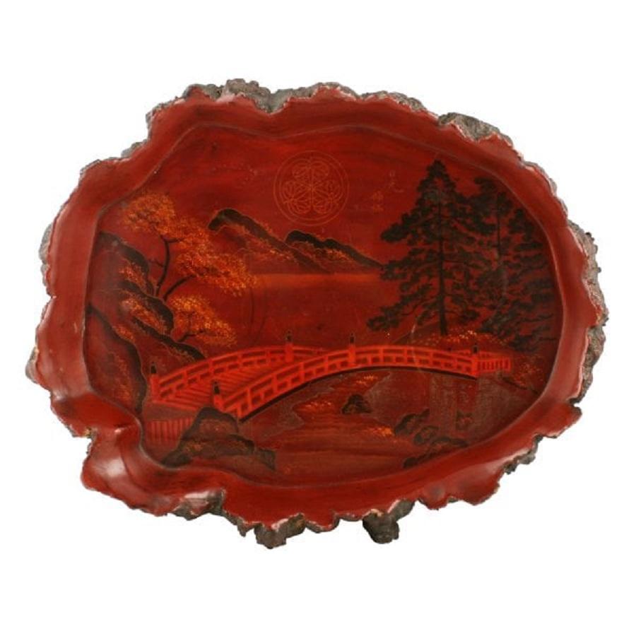 A late 19th century Japanese Meiji period red lacquered root wood tray.

The tray has a naturalistic root wood edge with a red lacquer to the inside that is decorated.

The tray has a scene of trees and water with a bridge in the centre,