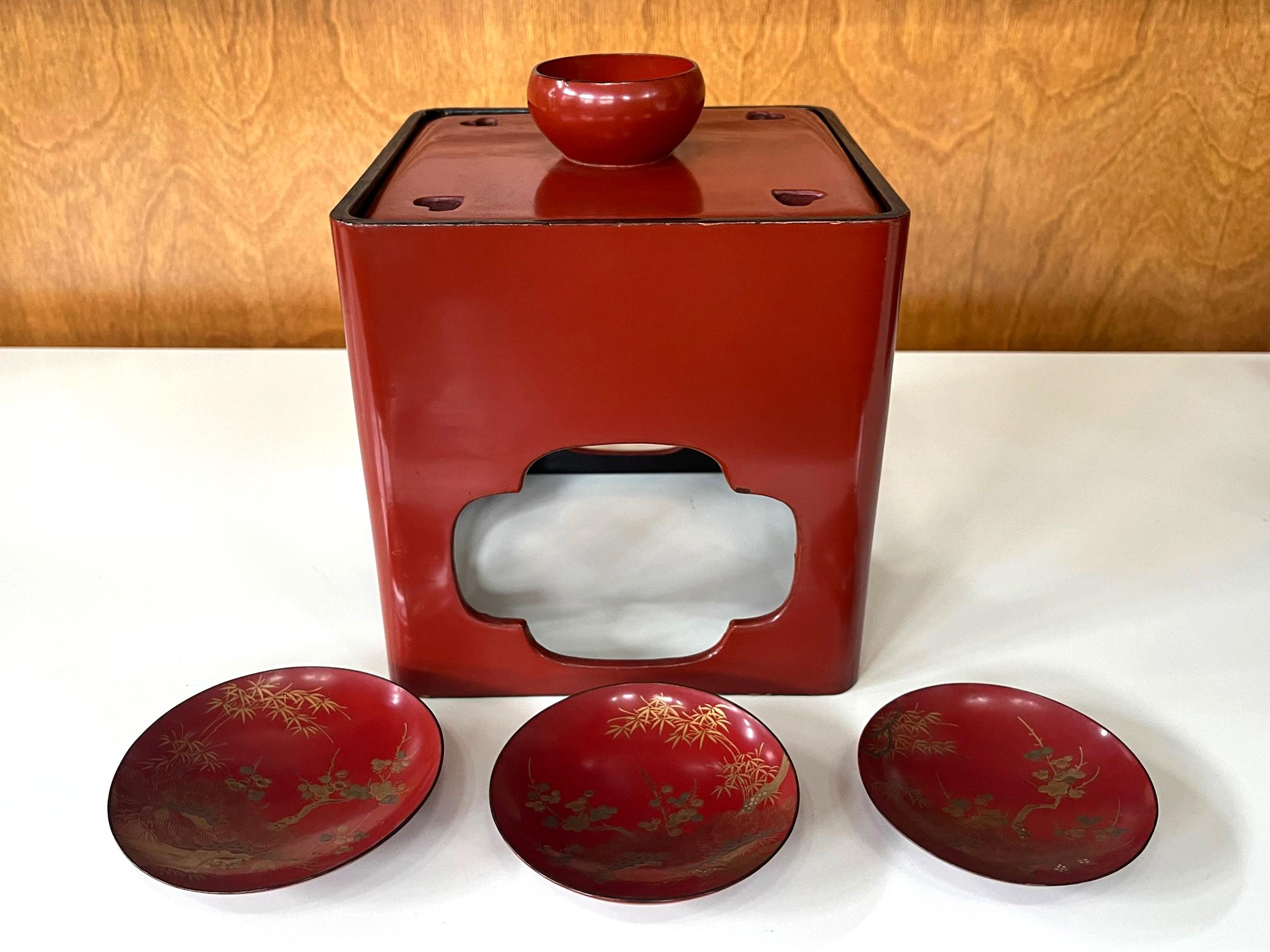 A Japanese lacquered Sake Drinking set circa late 19th century (end of Meiji period), The assemble consists of a red lacquer stand open frame support and a lid that encloses a storage space with black lacquered interior. The lid features a and a cup