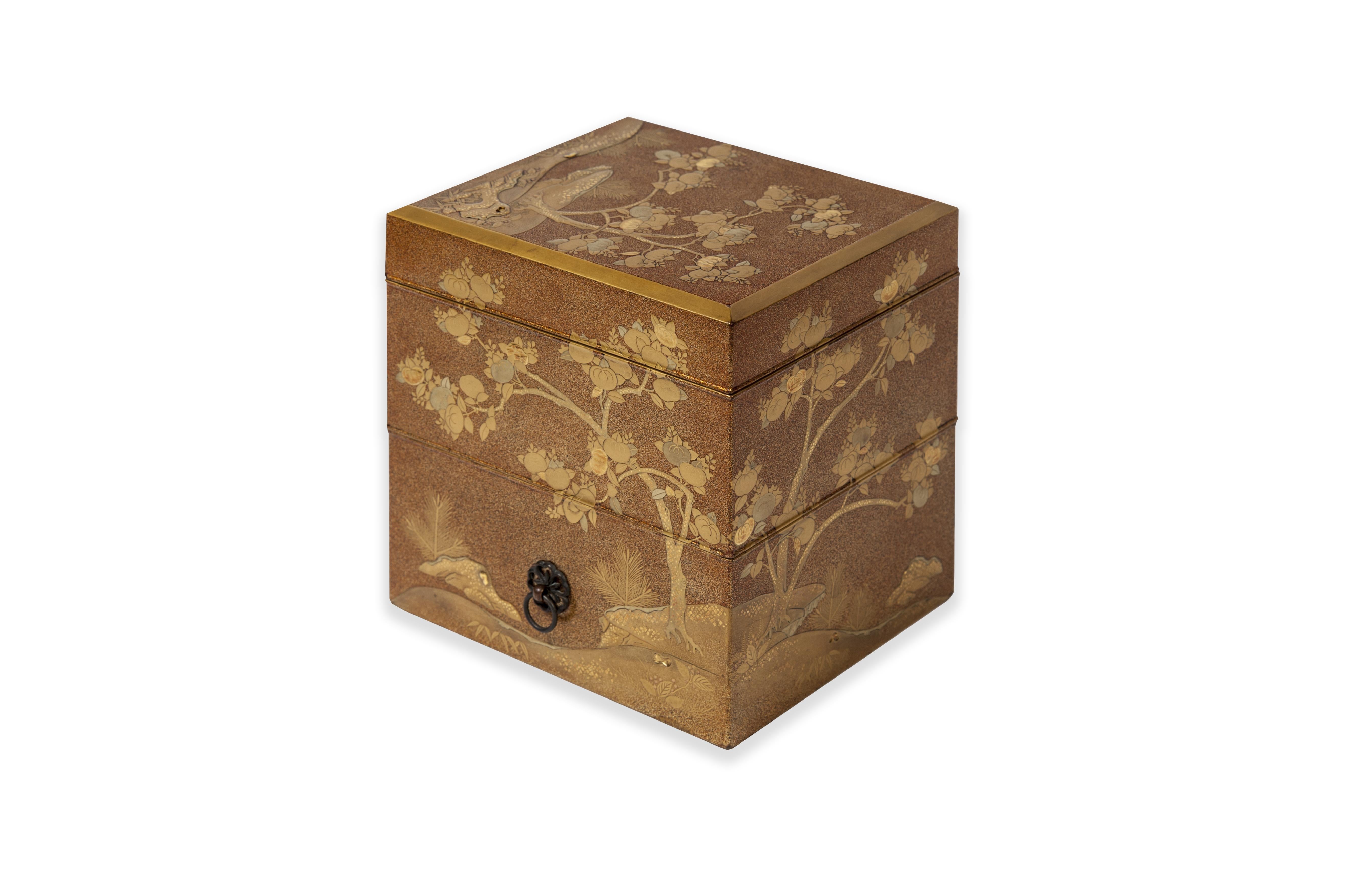 Tebako box with three compartments in golden and nashi-ji lacquer, decorated with golden, red, and kirigane lacquer, golden persimmon tree leaves, among rocks. The compartments are of increasing size from the top. The decoration is in continuity.