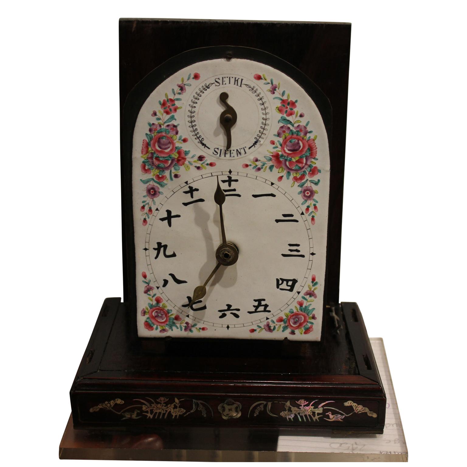 Inlay Japanese style clock. The clock has a Porcelain face that is hand painted with flowers. Flowers and birds are inlaid in the wood. There are glass panes and a glass door that opens up to reveal the face. The top of the clock comes off to reveal