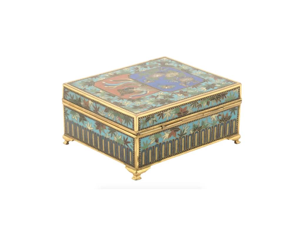An antique Japanese footed copper trinket box of rectangular form with hinged lid. Late Meiji period, before 1912. The item is richly decorated with cloisonne enamel bamboo leaf ornaments. Depictions of a peacock and butterfly garnish the lid. The