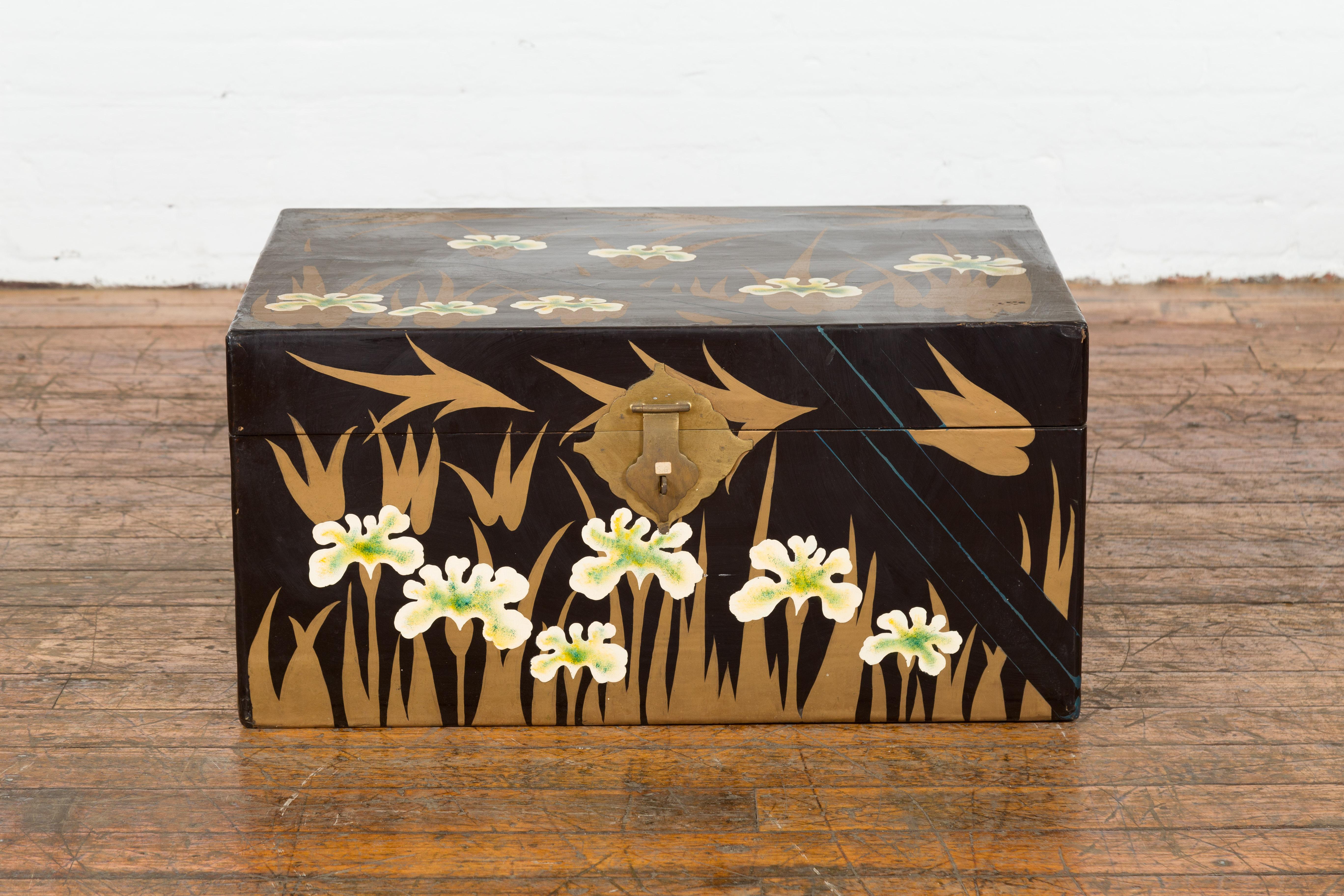 An antique Japanese late Meiji period black lacquer blanket chest from the early 20th century, with gold, white and green floral décor, brass hardware and blue painted accents. Created in Japan during the late Meiji period in the early 20th century,