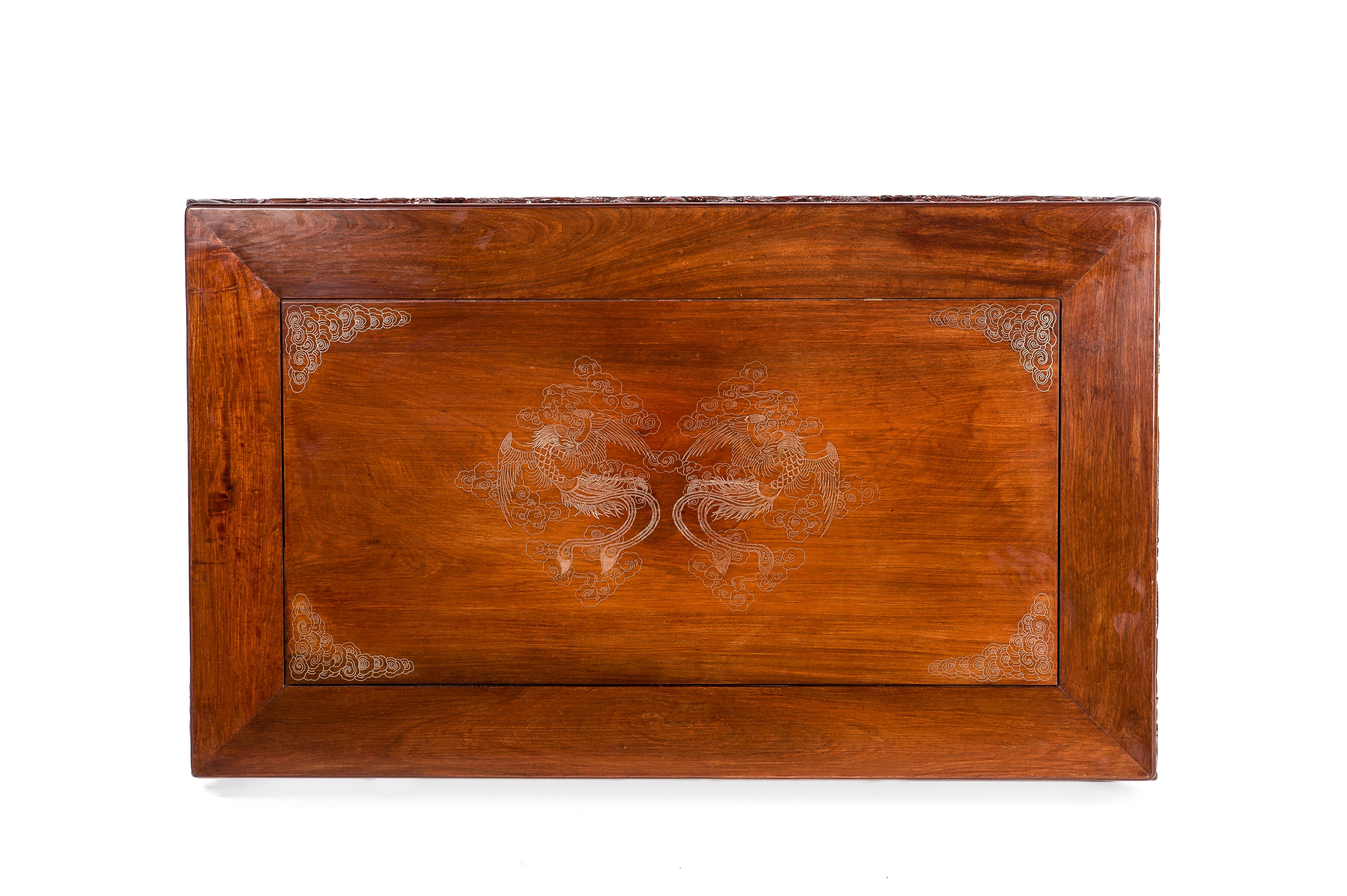 An elegant rectangular coffee table or opium table made in solid mahogany with beautiful grain.
The table has a rectangular paneled top with delicate inlaid silver wire figures. In the center, it shows two phoenixes in the clouds flanked by clouds