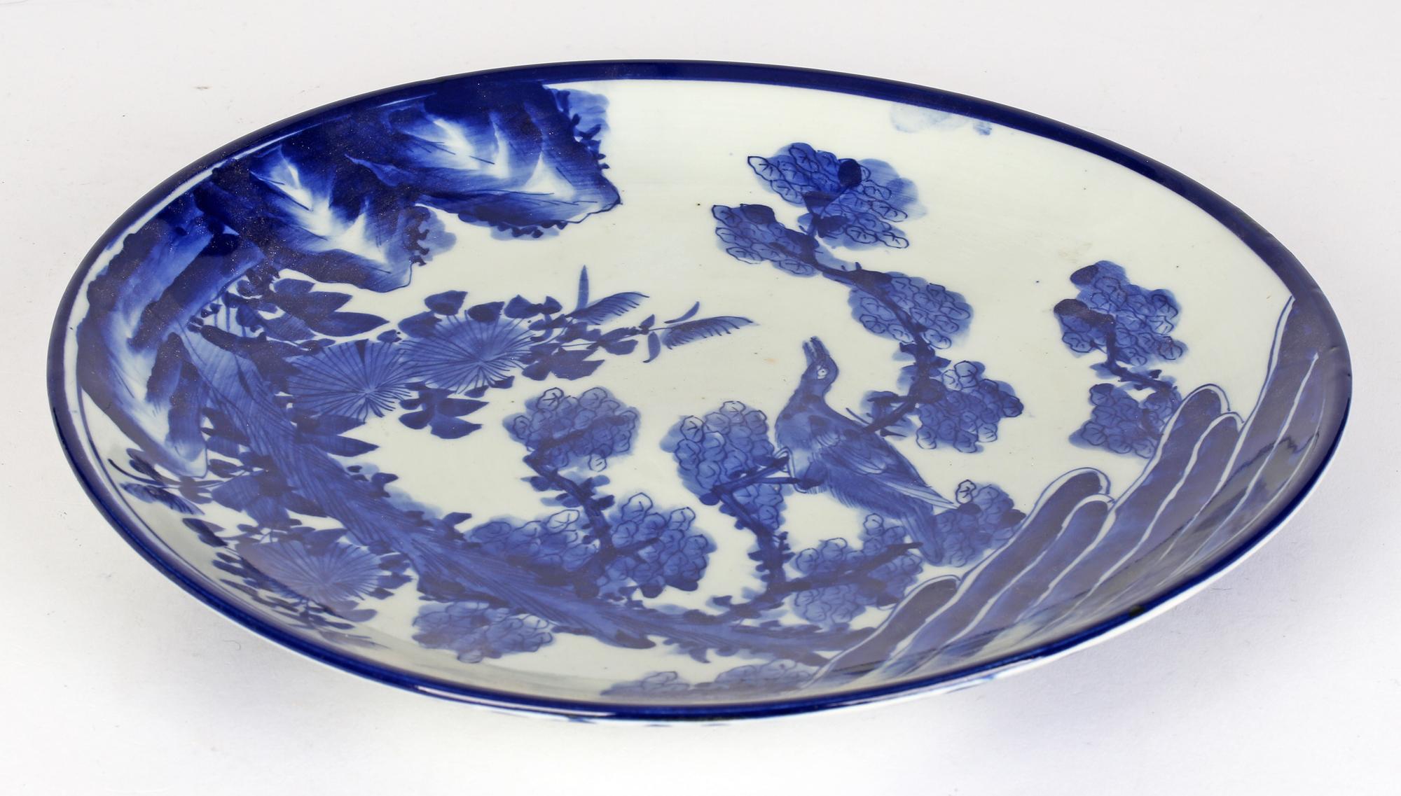 A fine decorative antique Japanese Meiji period porcelain plate hand painted with a bird in a landscape dating between 1868 and 1912. The large round plate with a slightly raised rim is hand painted in blue on a white ground with a large bird