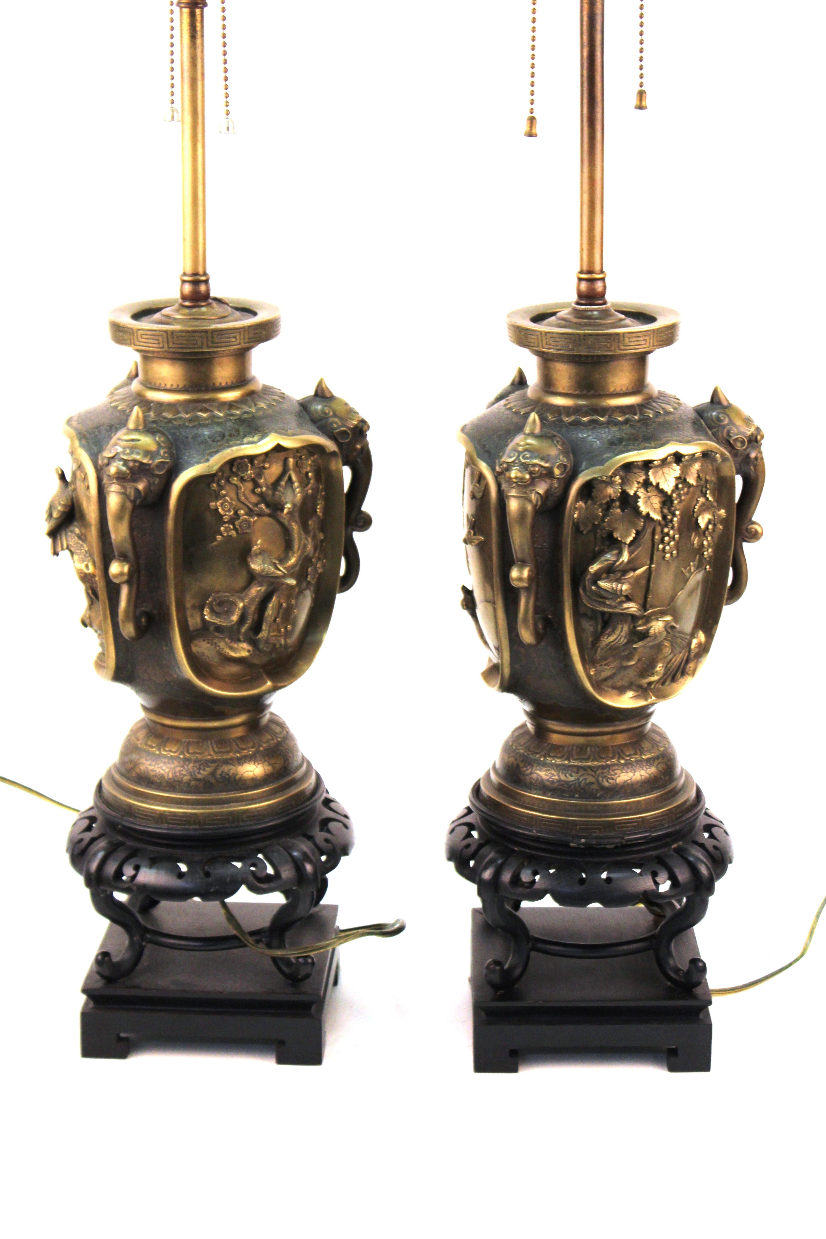 Japanese Meiji period bronze urn form table lamps. Each urn with three horned beast handles and relief animal and landscape scenes. Each has a decorative Ming-Xuande reign mark. The pair has been cleaned, causing a loss to the original applied
