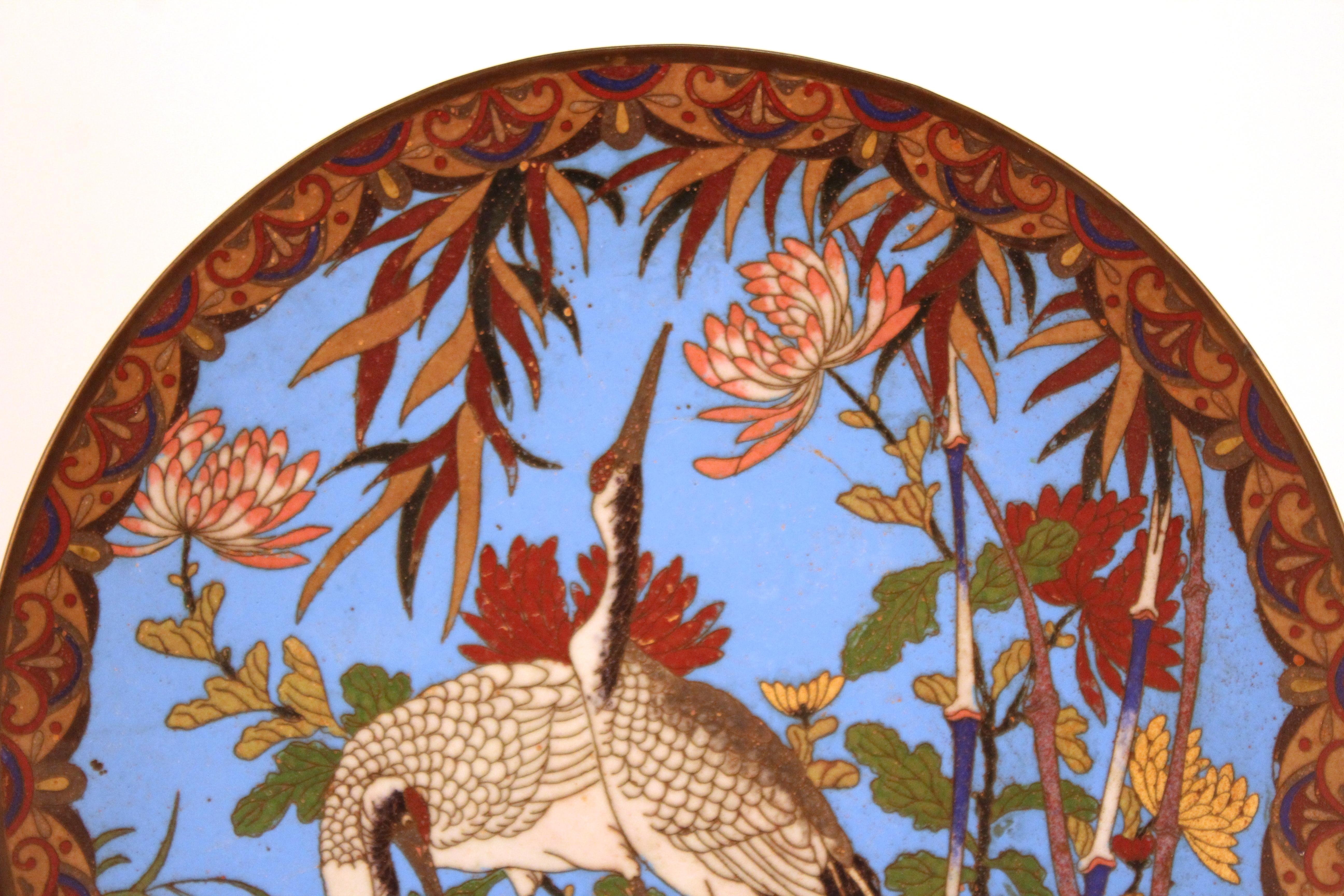 Japanese Meiji period plate with colorful cloisonne enamel, depicting two cranes and a chrysanthemum pattern on the border. The piece has a blue enameled back side and was made in circa 1900. In great antique condition with age-appropriate wear and