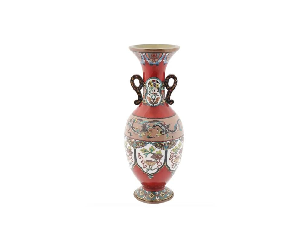 An antique Japanese Meiji Era Silver wire and enamel vase. Circa: late 19th century t. Unsigned. The amphora shaped vase is enameled with polychrome floral, foliage, scrollwork butterfly, and dragon patterns made in the Cloisonne technique on red