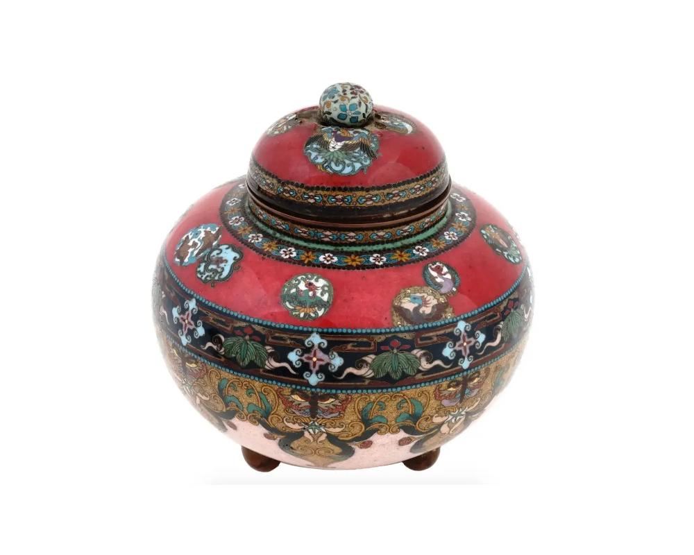 An antique Japanese, late Meiji Era, covered tripod enamel over brass koro type jar. The ware is adorned with polychrome medallions depicting Phoenix birds, floral, foliage butterfly, and scrollwork patterns made in the Cloisonne technique. The