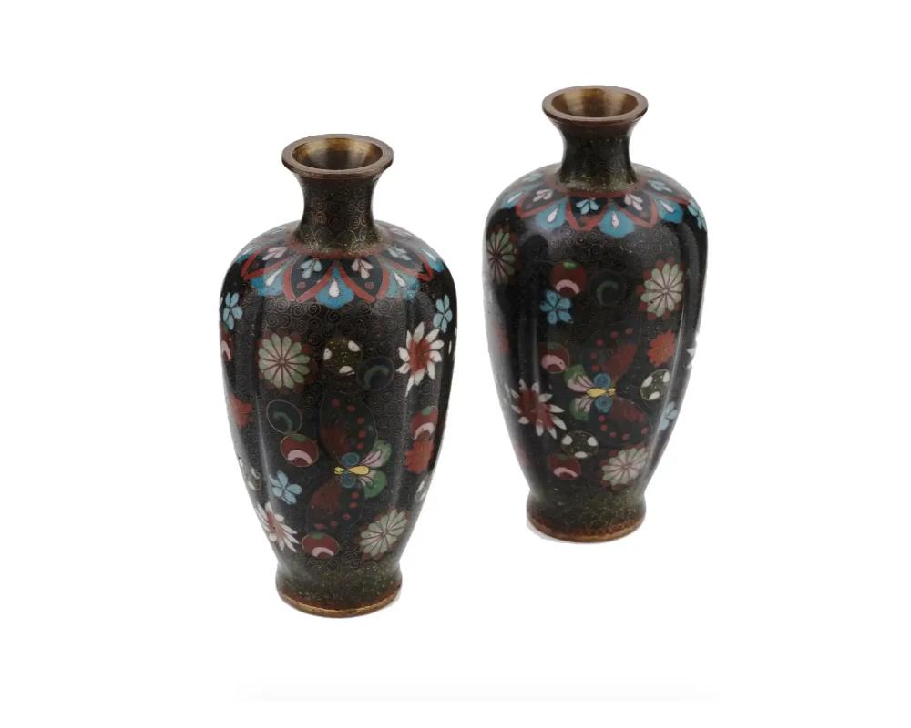 A pair of symmetrical antique Japanese, late Meiji era, amphora shaped enamel over brass vases. The exterior of the vases are enameled with polychrome images of blossoming flowers and butterflies, floral, foliage, geometrical, and swirl patterns,