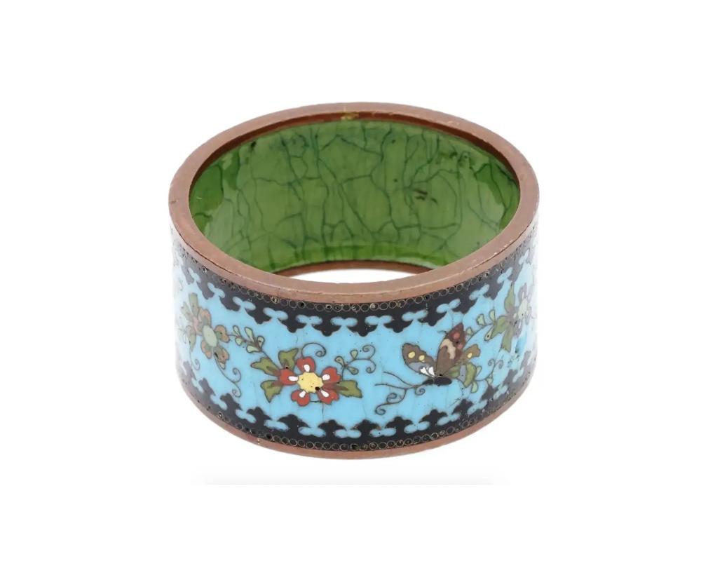 An antique Japanese Meiji Era copper and enamel napkin ring. Circa: early 20th century. The ware is enameled with polychrome floral, foliage, and butterfly patterns made in the Cloisonne technique. Unmarked. The borders are enameled with black