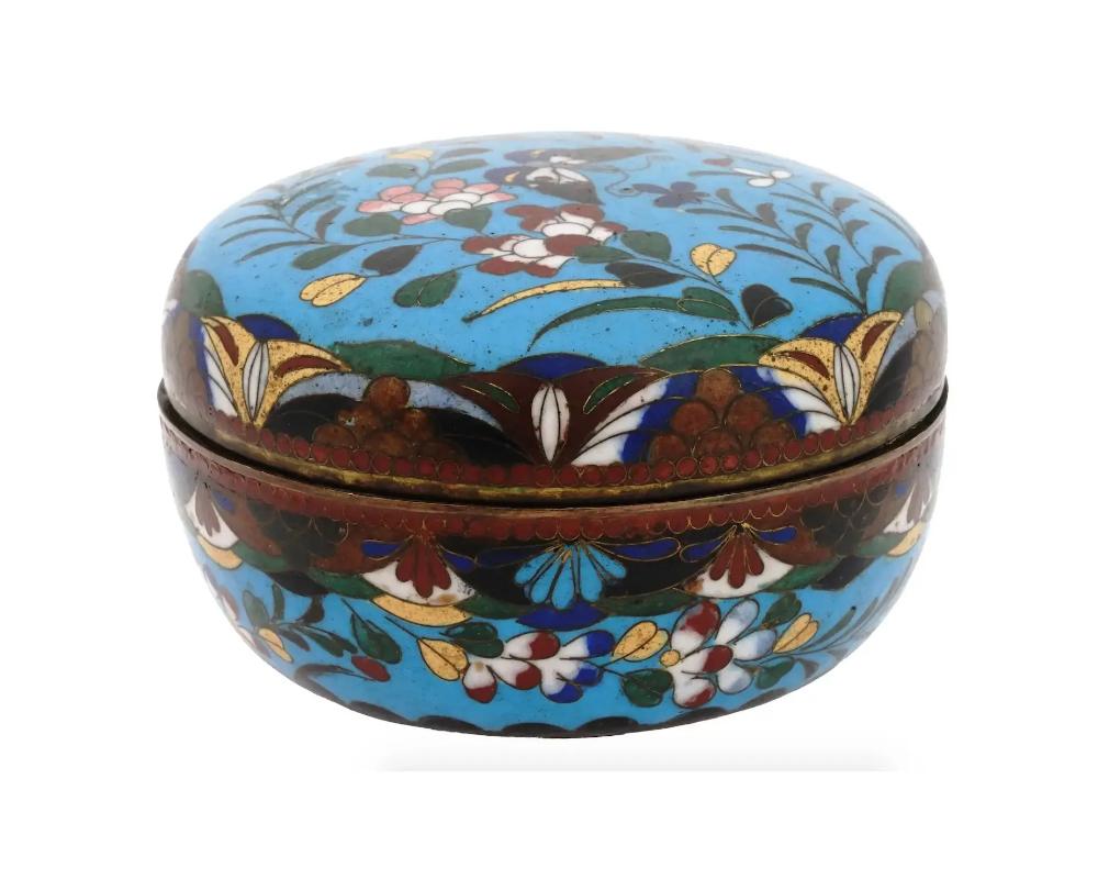 An antique Japanese round copper trinket box with cloisonne enamel design. Late Meiji era, before 1912. The piece is decorated with flowers and butterfly motid against the turquoise blue background. Collectible Oriental Vanity Items And