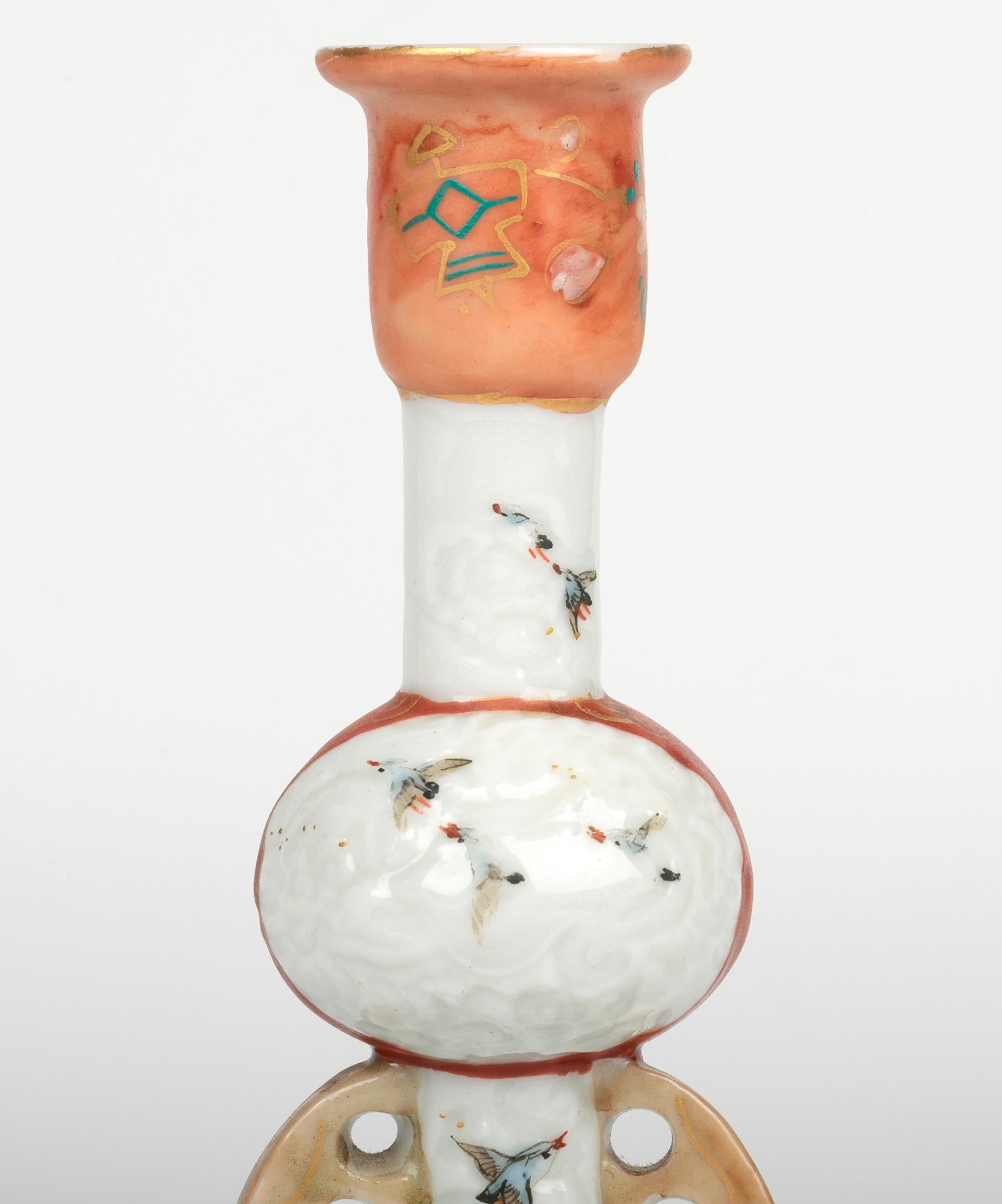 A stylish Japanese antique Kutani candlestick hand-painted with birds dating from the Meiji period 1868-1912. The porcelain candlestick stands on a wide rounded base with a narrow tall central round knop stem with looped handles applied either side