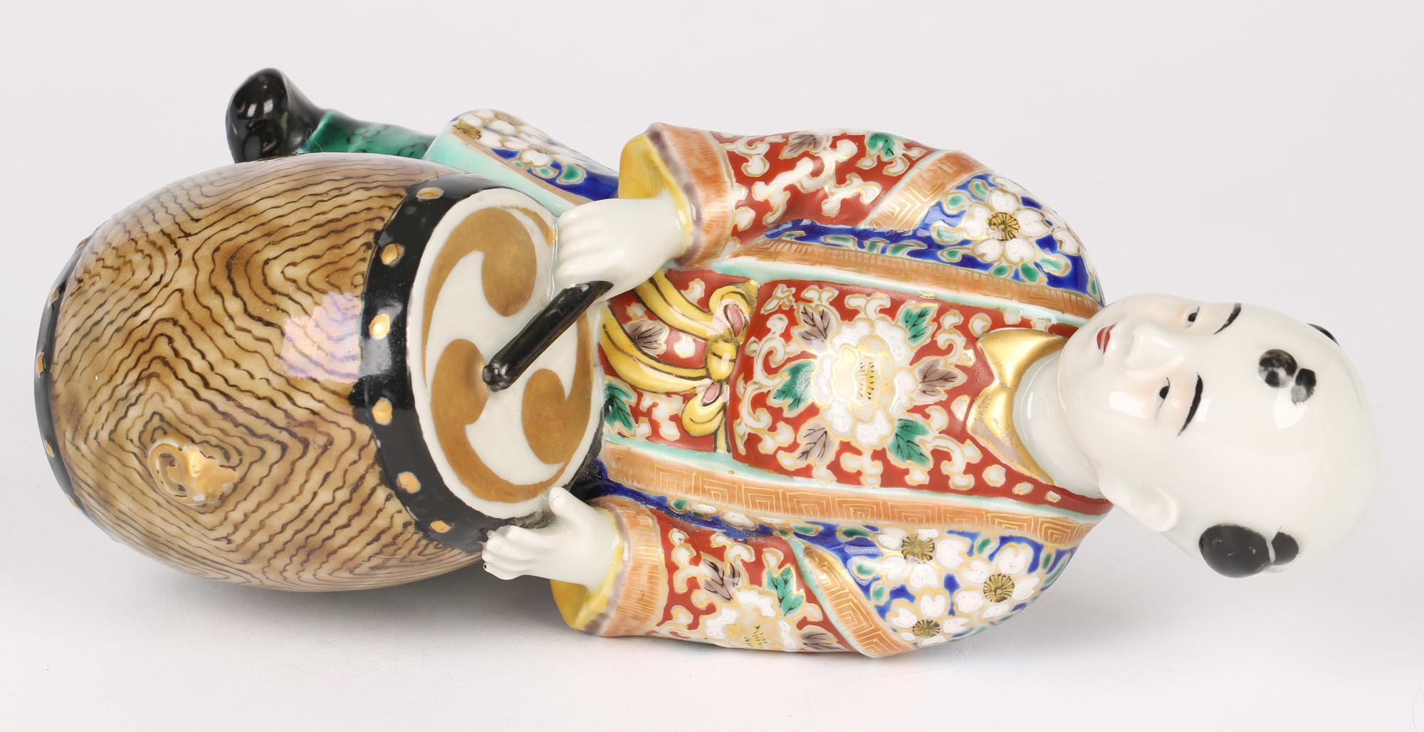 A deligthful antique Japanese Kutani porcelain figure of a drummer boy dating from the Meiji period 1868 to 1912. The figure is well modeled a long ornate jacket richly painted with floral designs in blues, reds and greens on a white ground and