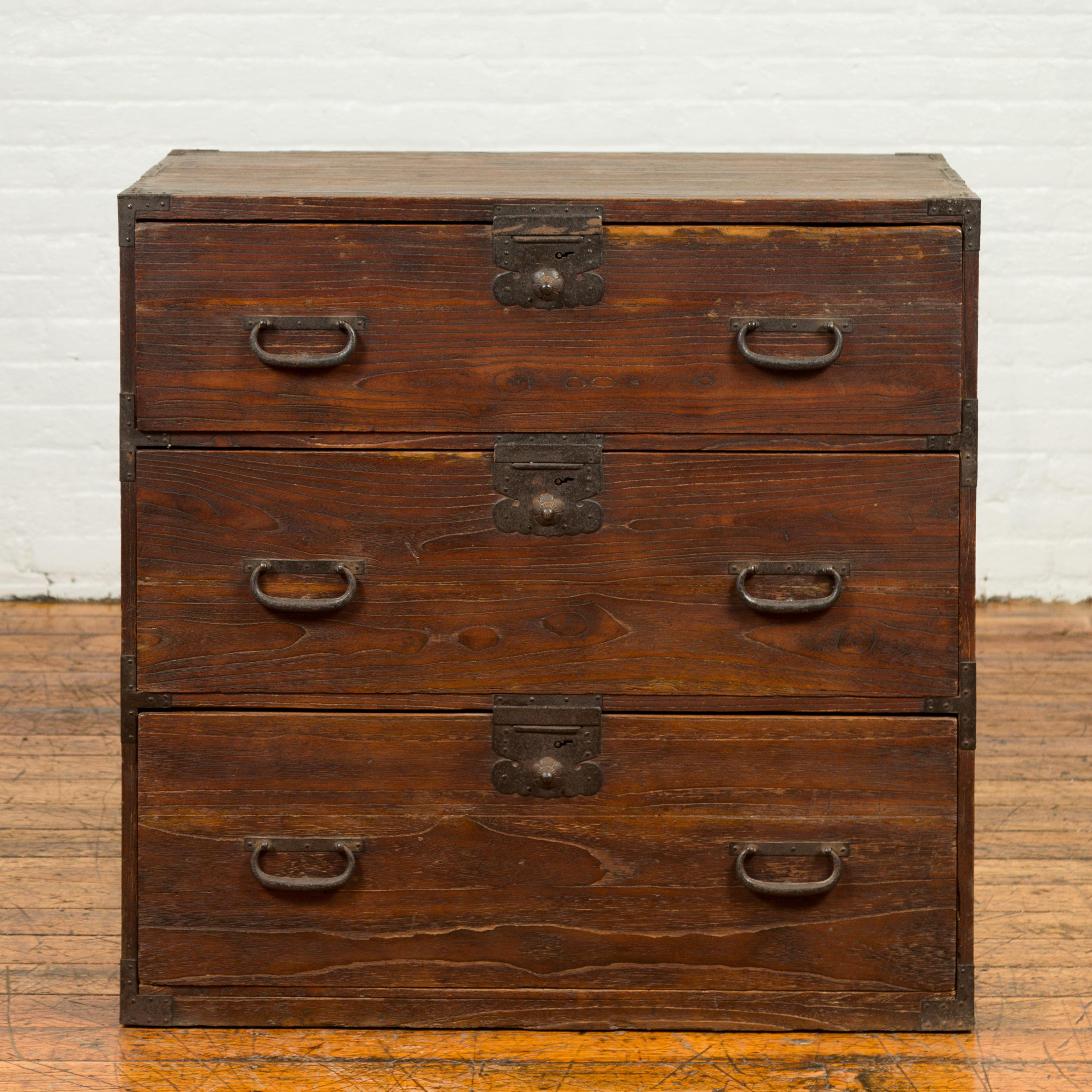 A Japanese Meiji period keyaki wood tansu clothing chest from the 19th century, with three drawers and iron hardware. Born in Japan during the Meiji period, this tansu traveling chest features a rectangular top sitting above three drawers each