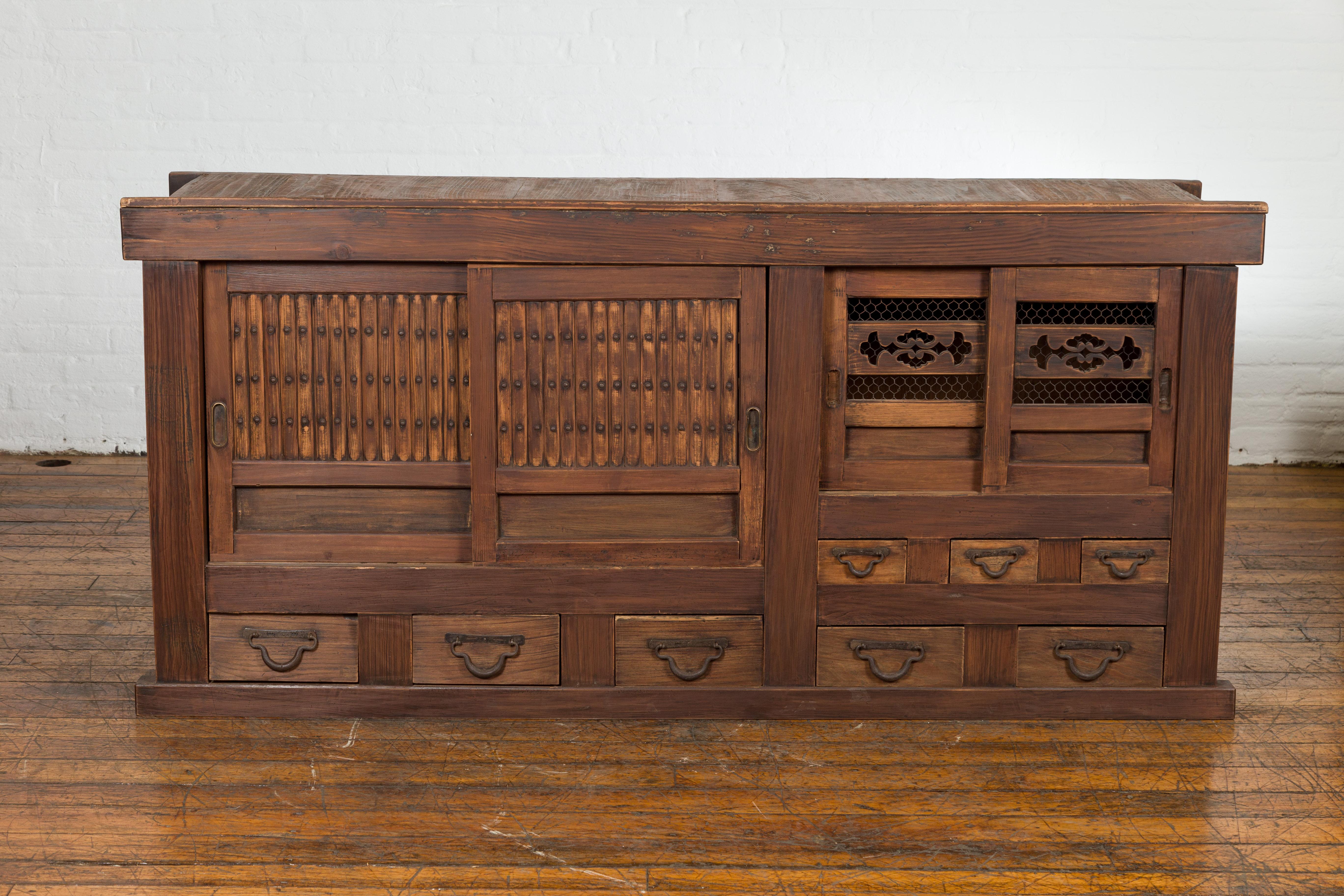An antique Japanese Meiji period Mizuya kitchen tansu cabinet from the 19th century, with two pairs of sliding doors, eight drawers, carved motifs and iron hardware. Created in Japan during the Meiji period in the 19th Century, this Mizuya kitchen