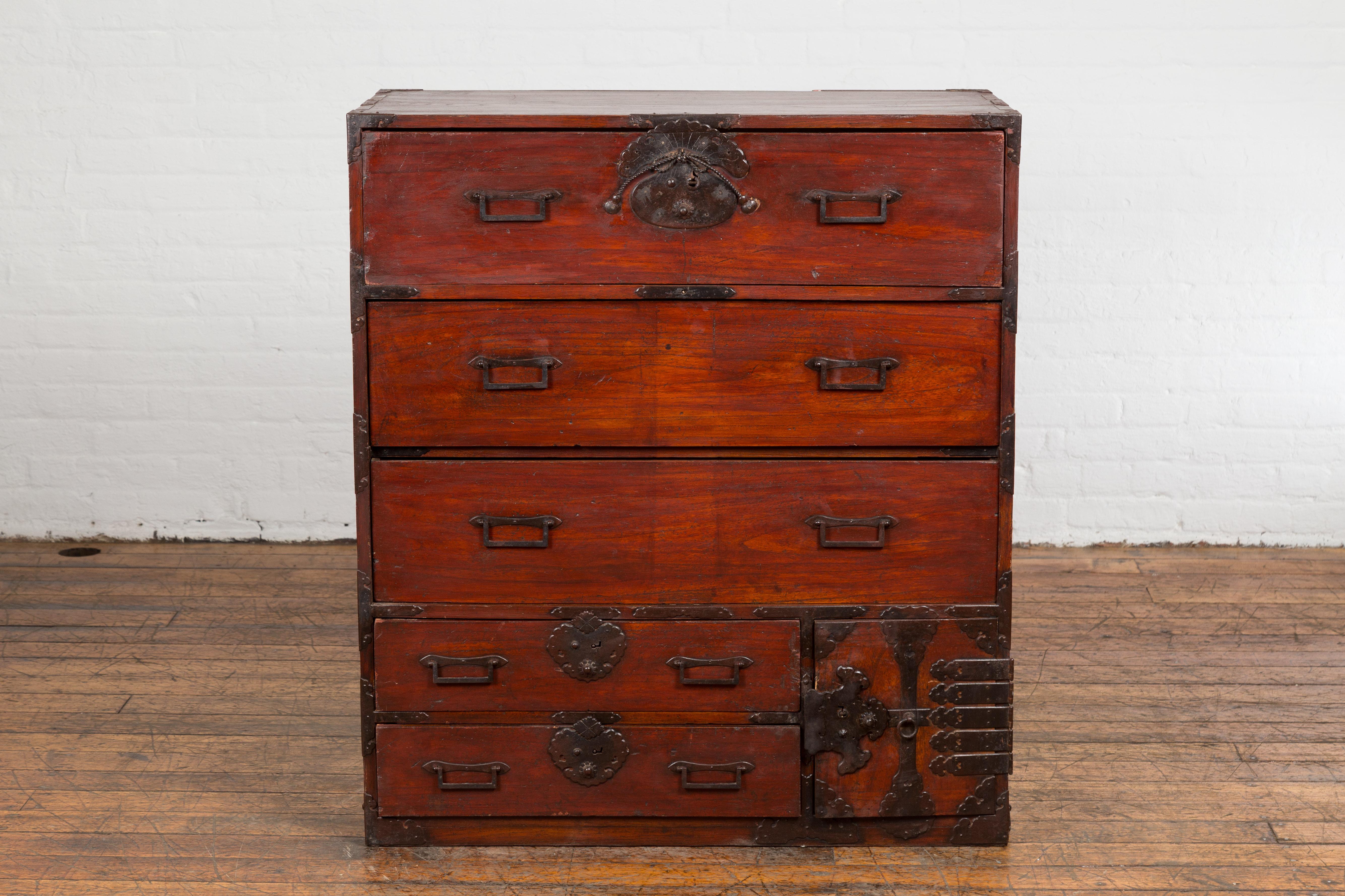 A Japanese Meiji period Isho Dansu clothing chest from the 19th century with reddish brown lacquer, iron hardware, five drawers and a side door revealing two additional hidden drawers. Exuding an aura of refined grace and practicality, this