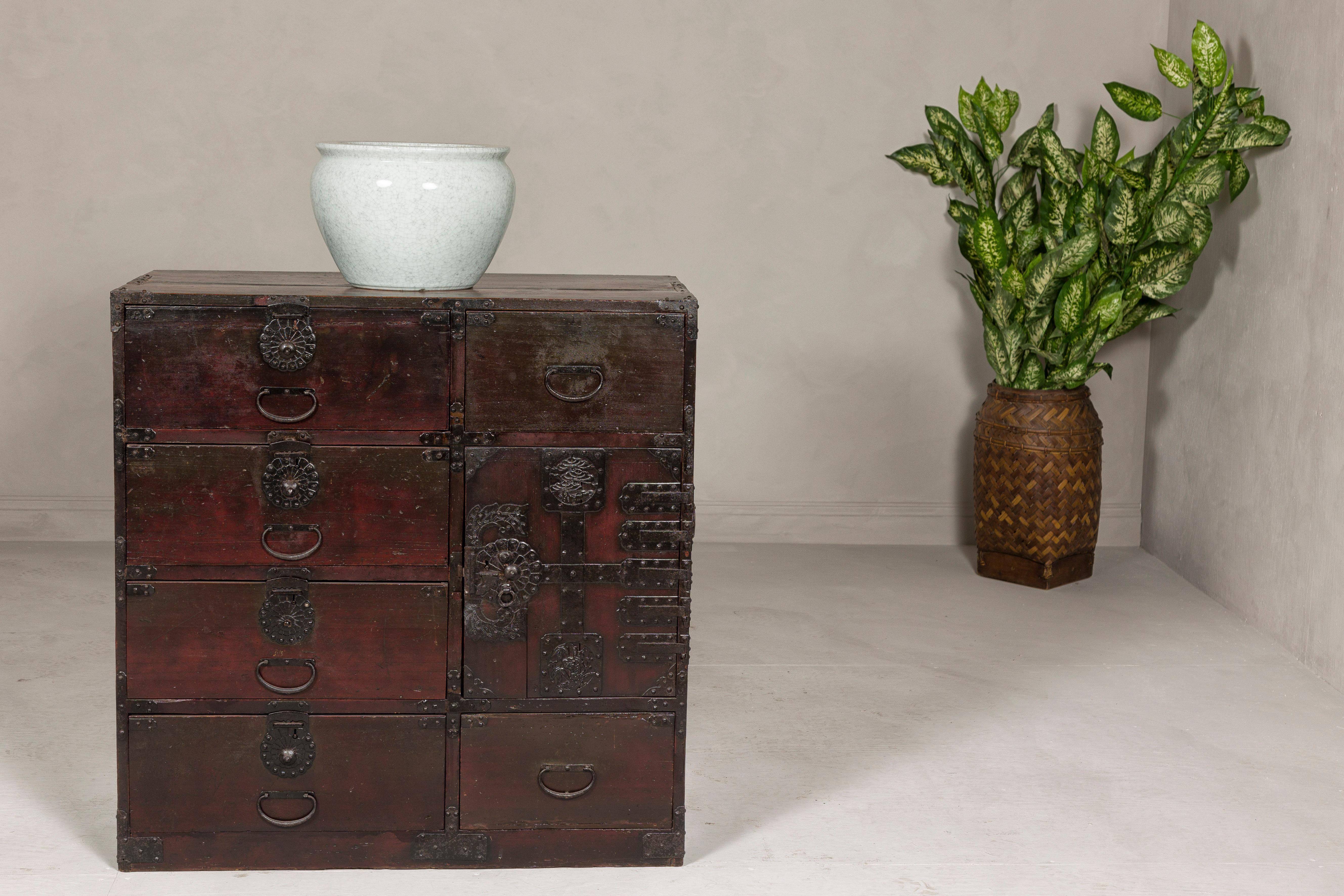 A Japanese Meiji period Sendai type tansu chest from the 19th century with ornate iron hardware, six exterior drawers and safe. Discover the intricate beauty and functional elegance of this Japanese Meiji period Sendai-type tansu chest, a piece from