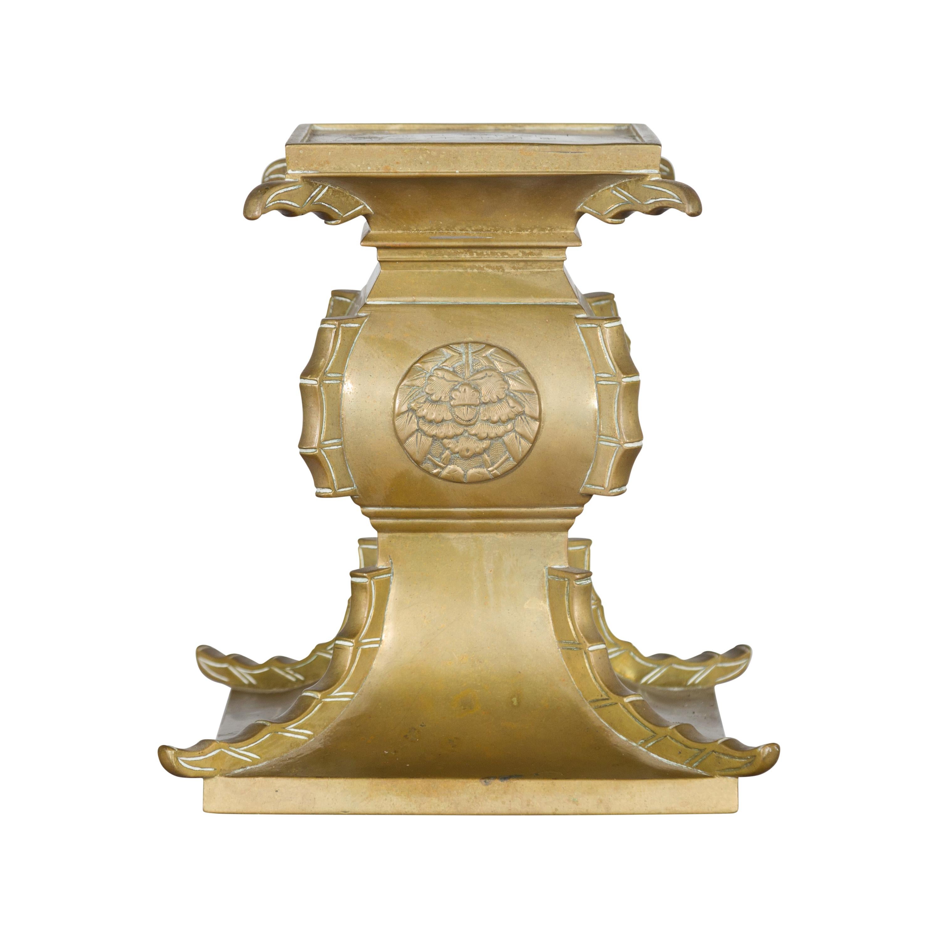 A Japanese Meiji period antique brass square top candle holder from the early 20th century, with intricate carved medallion, calligraphic inscription and ornate base. Created in Japan during the Meiji period in the early years of the 20th century,