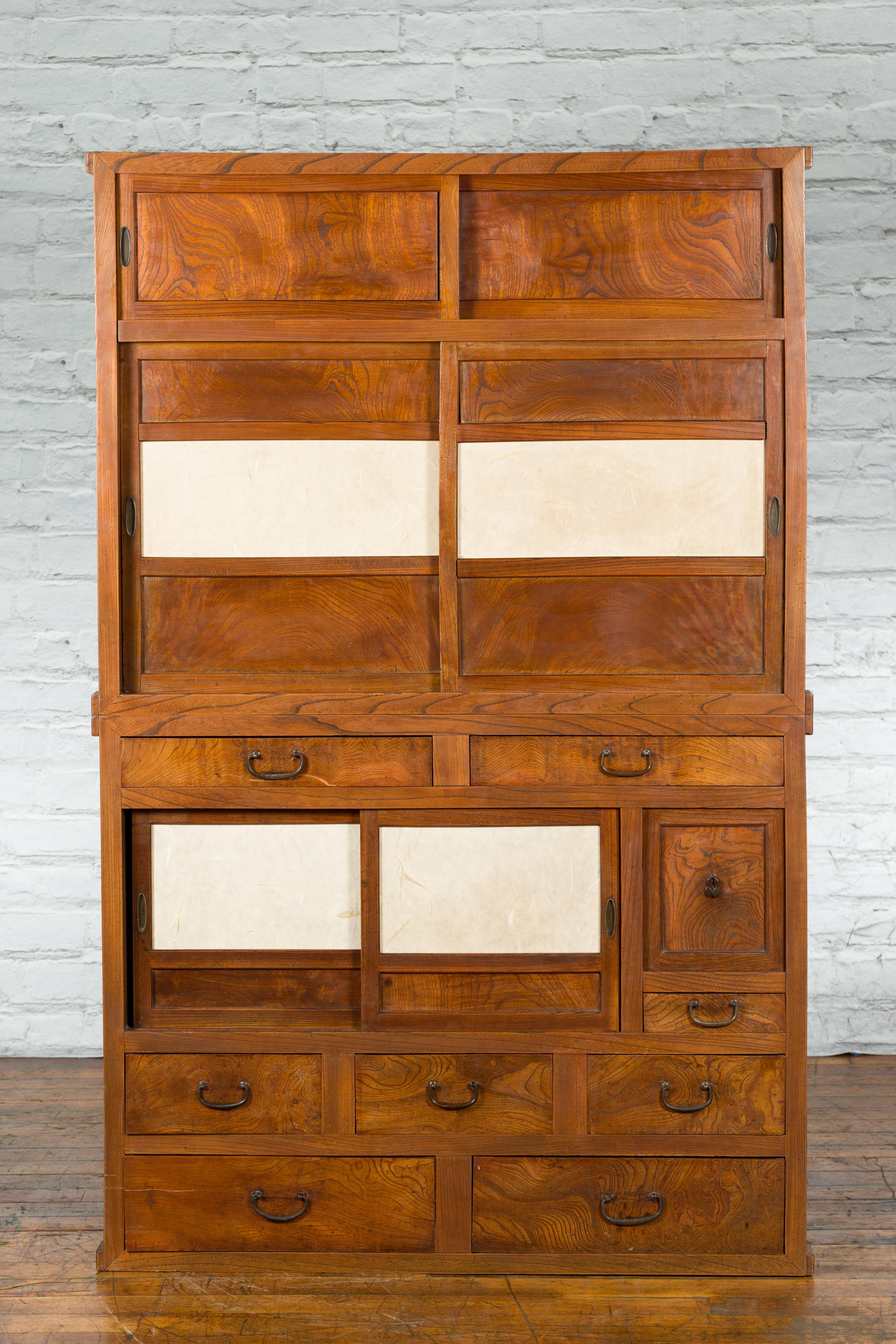A Japanese Meiji period kiri wood two-part kitchen cabinet in the Kanto style with sliding doors, parchment paper and drawers. Created in Japan during the Meiji era, this Kanto style kiri wood cabinet features a linear silhouette perfectly accented